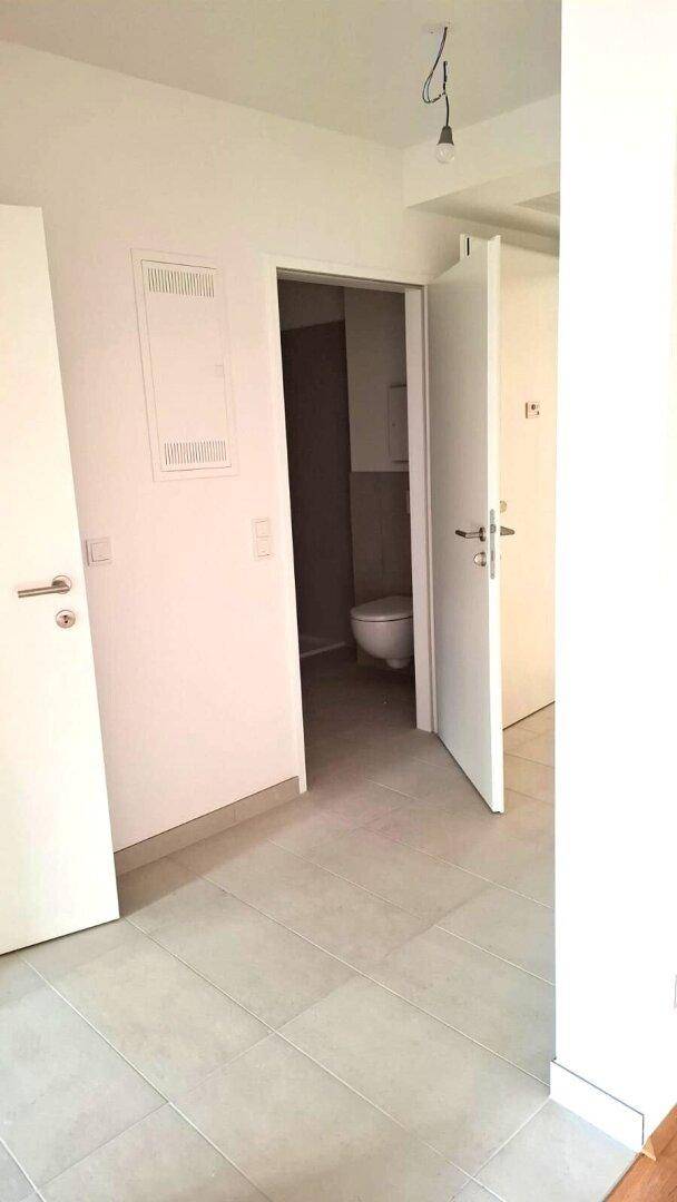 Flur mit Fliesenboden und Blick in ein angrenzendes WC, das durch eine offene Tür sichtbar ist.