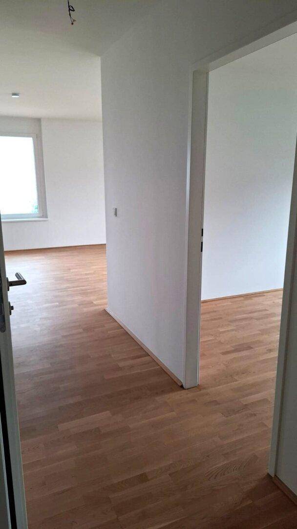 Geräumiger Raum mit hellem Parkettboden und einem großen Fenster, das viel Licht spendet.