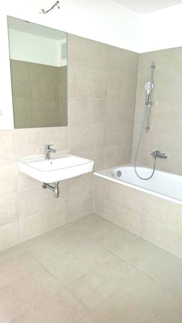 Modernes Badezimmer mit Badewanne, Waschbecken und Spiegel, ausgestattet mit beigefarbenen Fliesen.