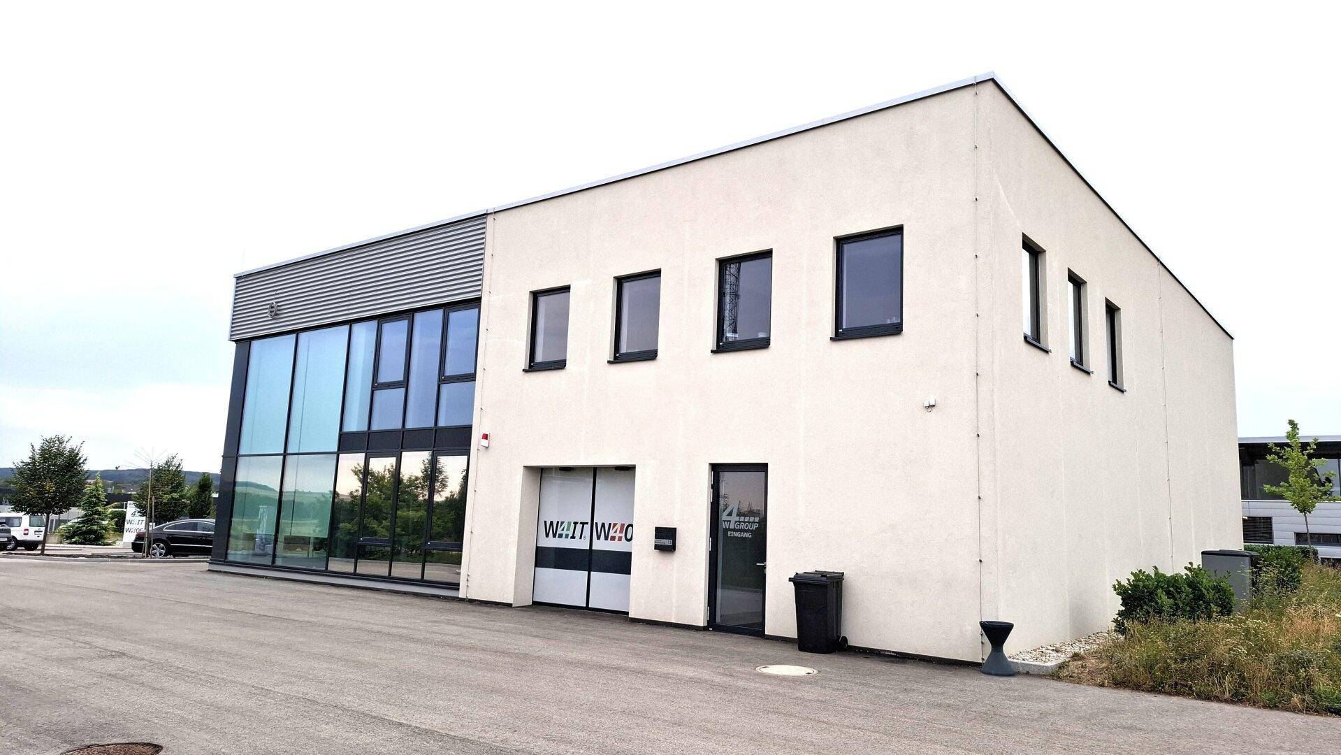 Seitenansicht des modernen Geschäftsgebäudes mit einer Kombination aus Glas- und Putzfassade sowie einem Garagentor.
