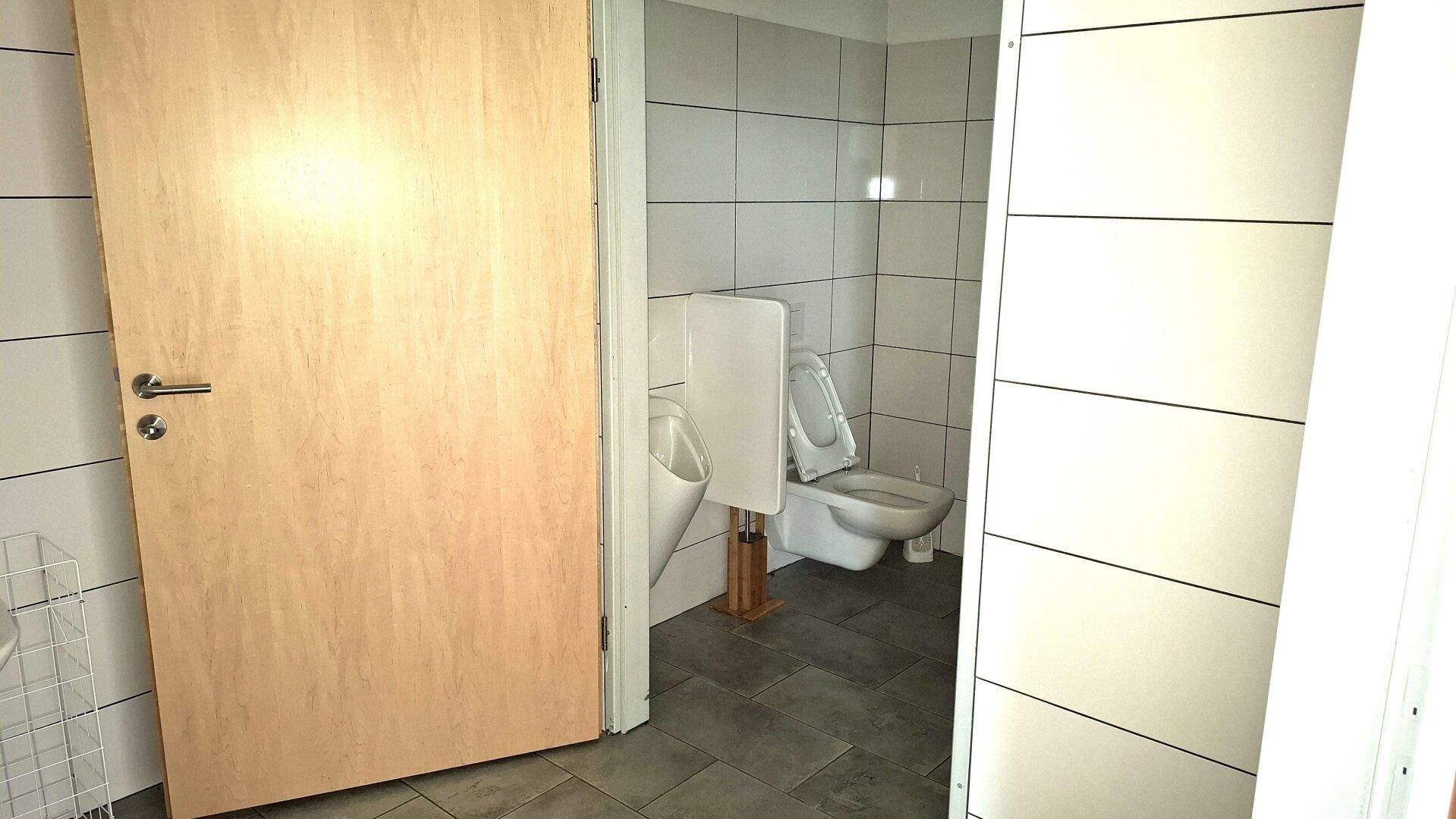 Modernes Badezimmer mit Fliesen an Wänden und Boden, ausgestattet mit Toilette und Urinal.