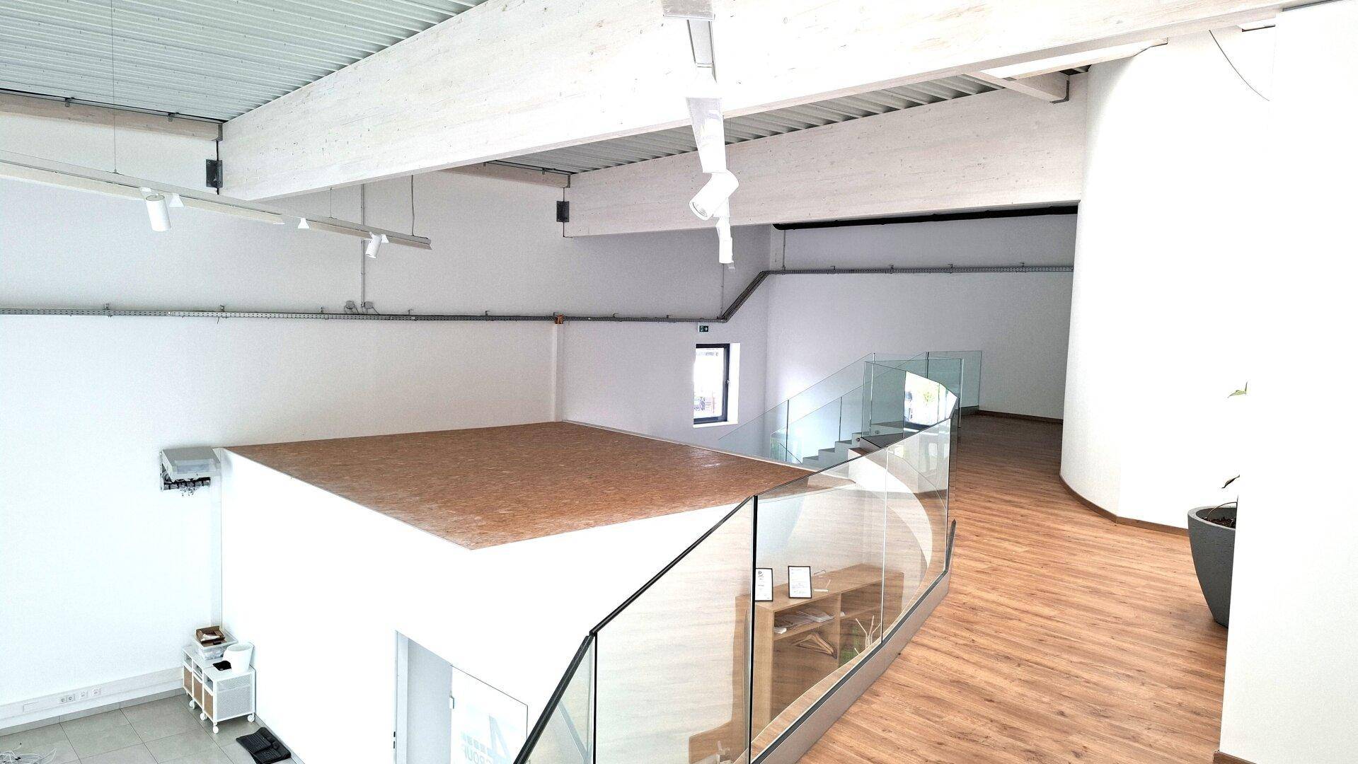 Offener Bereich im Obergeschoss mit Glasgeländer, Holzboden und sichtbaren Deckenbalken, der eine moderne Ästhetik zeigt.