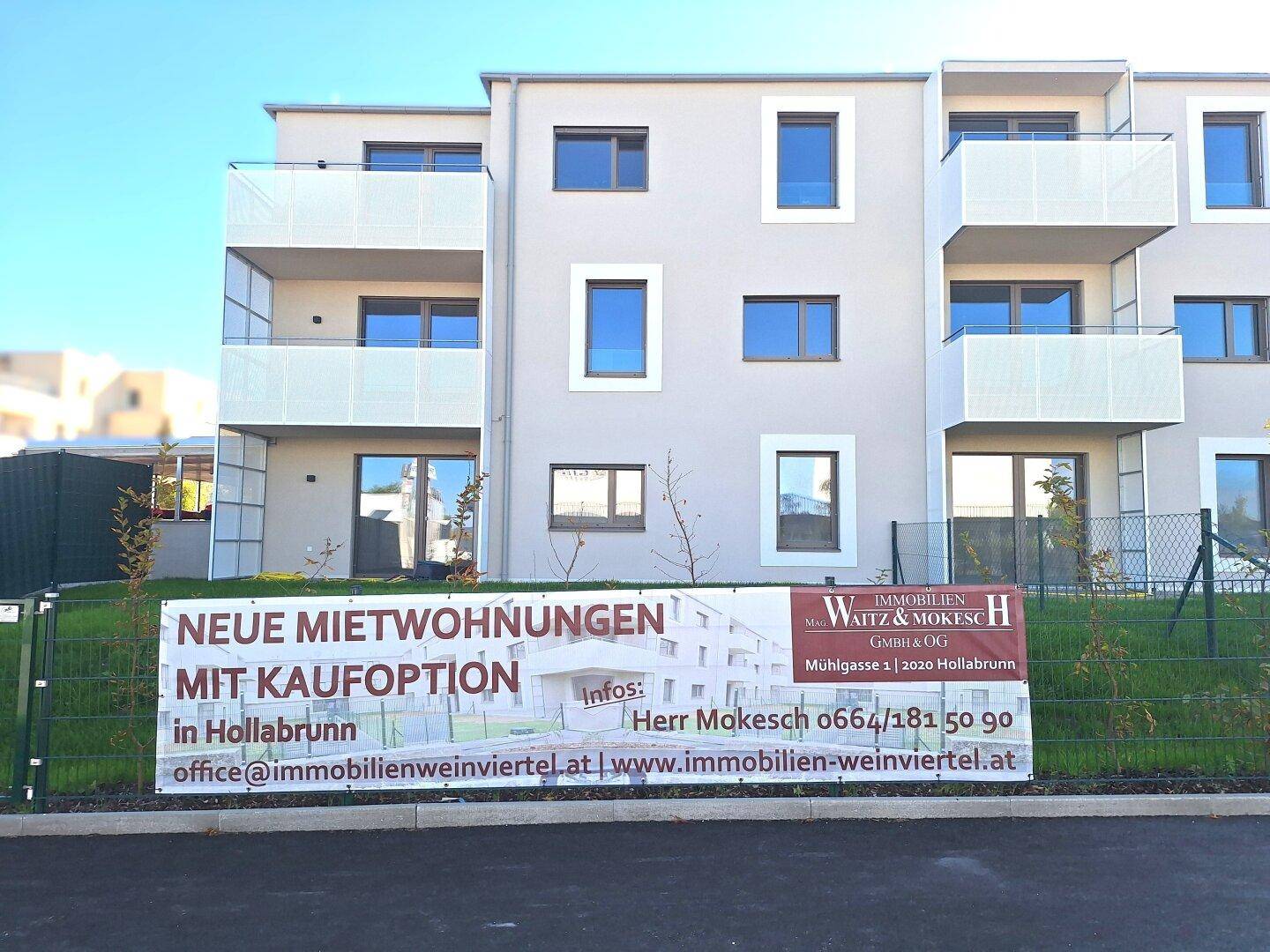 Nahaufnahme eines modernen Wohngebäudes mit Balkonen und großem Werbebanner.