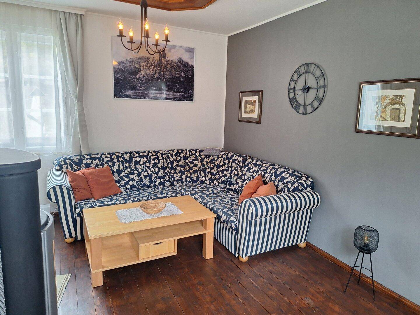 Detailansicht des Wohnzimmers mit bequemem Ecksofa, Holztisch und dekorativer Wanduhr an der Akzentwand.