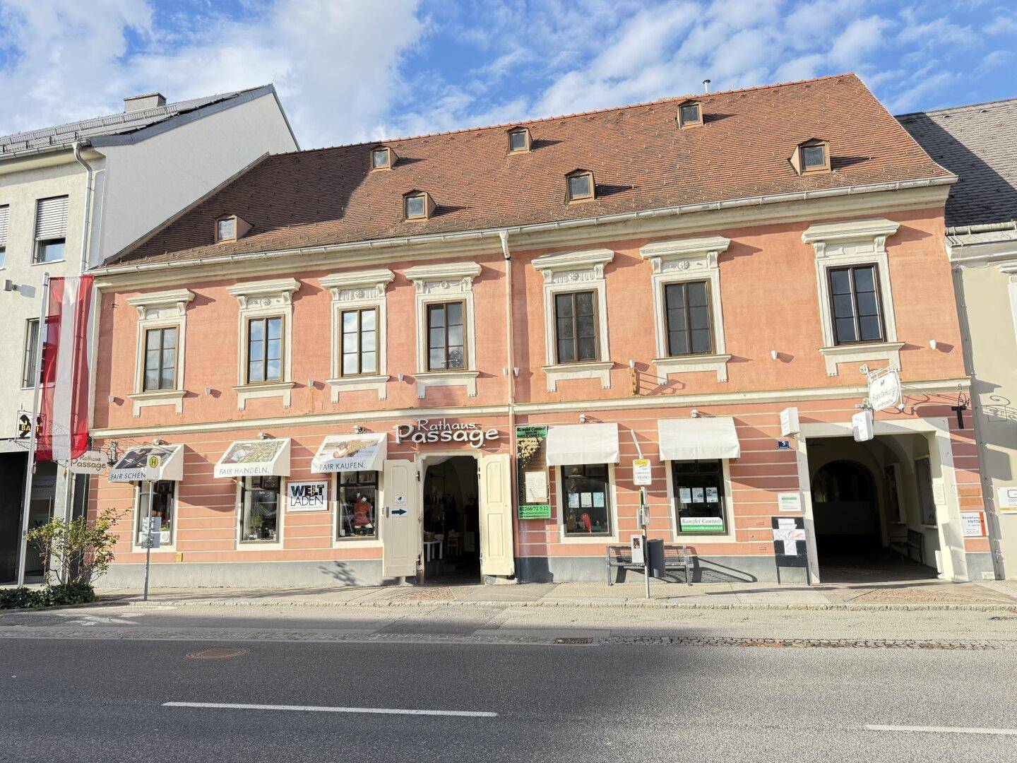 Ansicht des historischen Gebäudes mit rosa Fassade und Geschäften an einer belebten Straße.