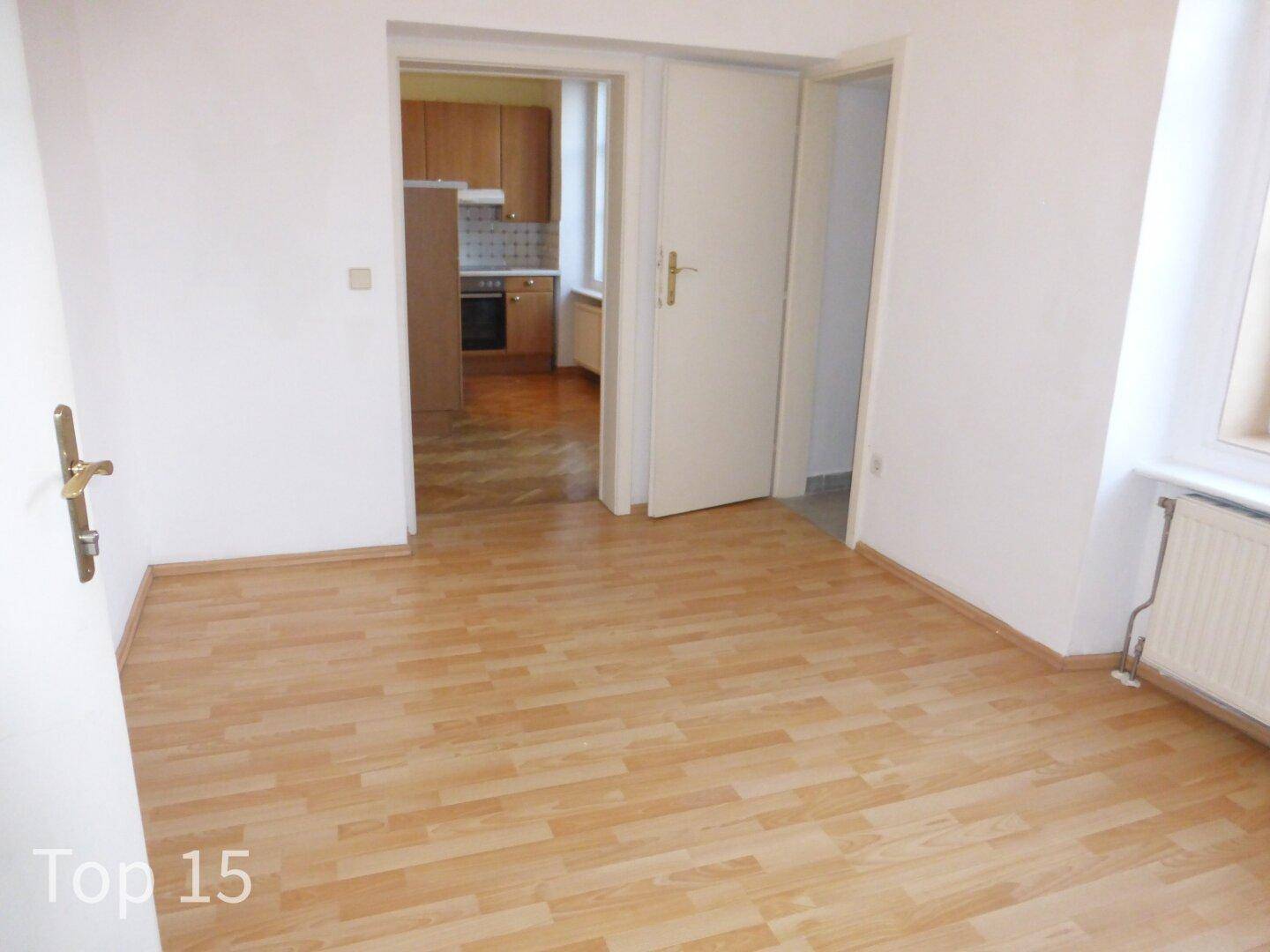 Helles Wohnzimmer mit Laminatboden und Zugang zu einer separaten Küche.