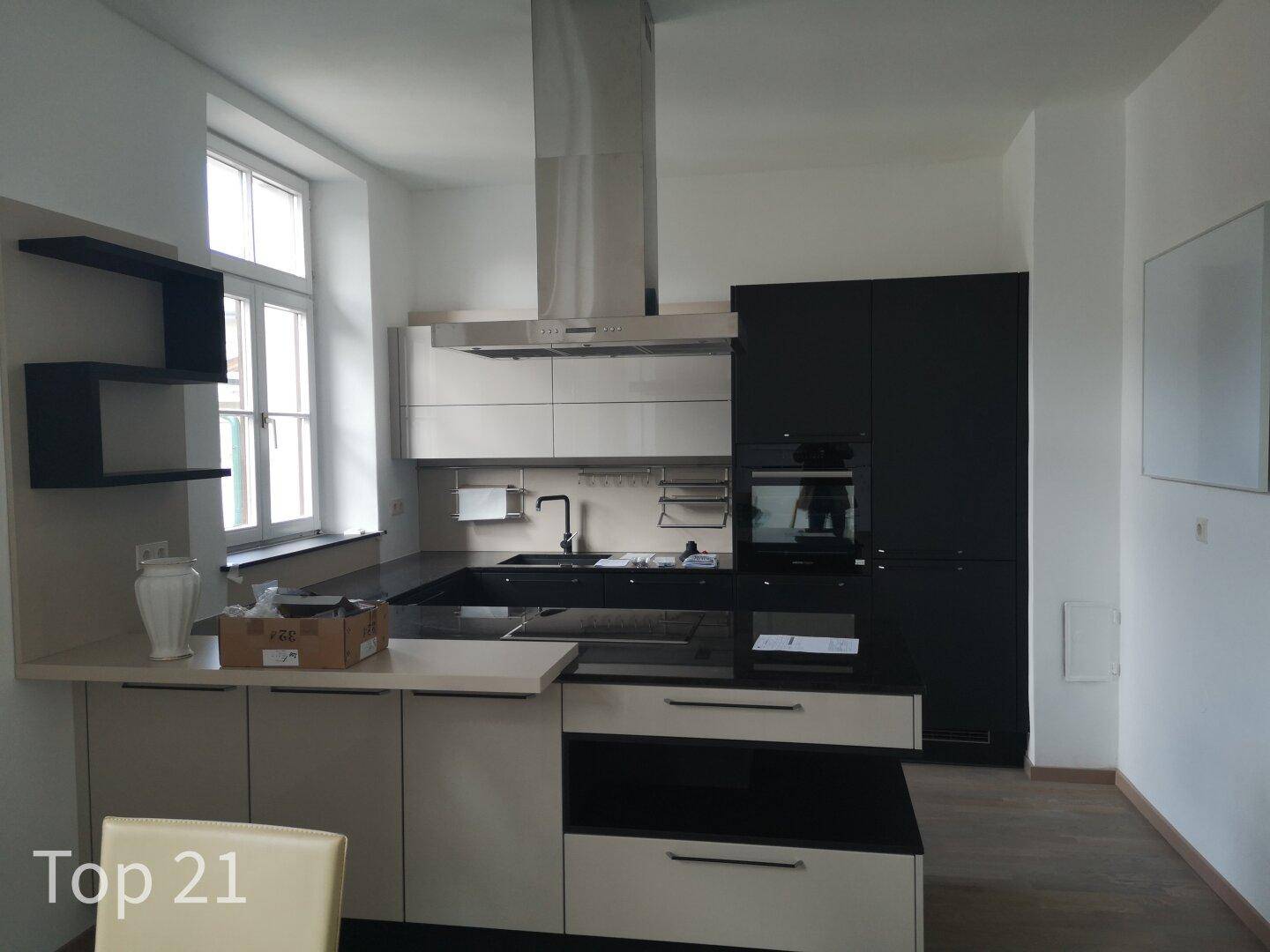 Moderne Küche mit schwarzen und beigen Schränken, Dunstabzugshaube und großem Fenster.
