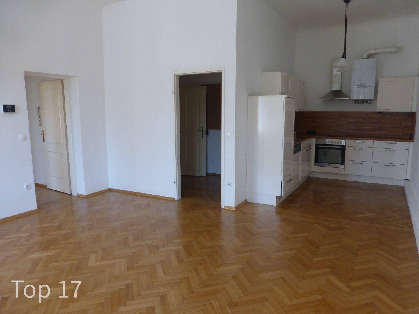 Offener Wohnbereich mit Parkettboden und integrierter weißer Küchenzeile.