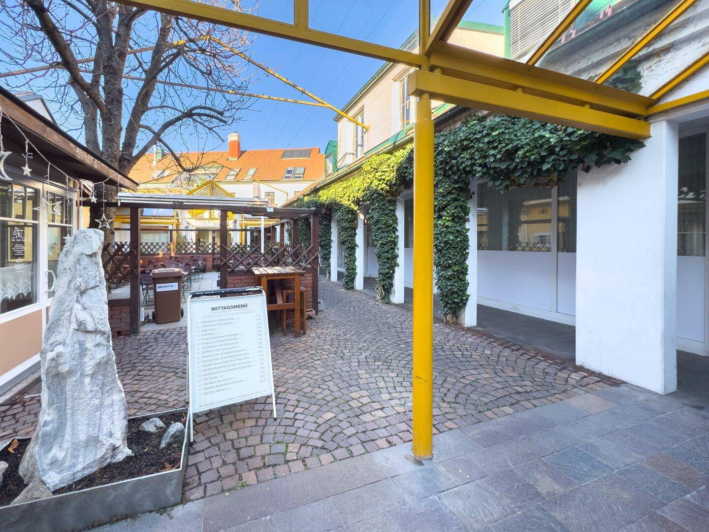 Gemütlicher Innenhof mit Kopfsteinpflaster, Pflanzen und Sitzgelegenheiten im Freien.