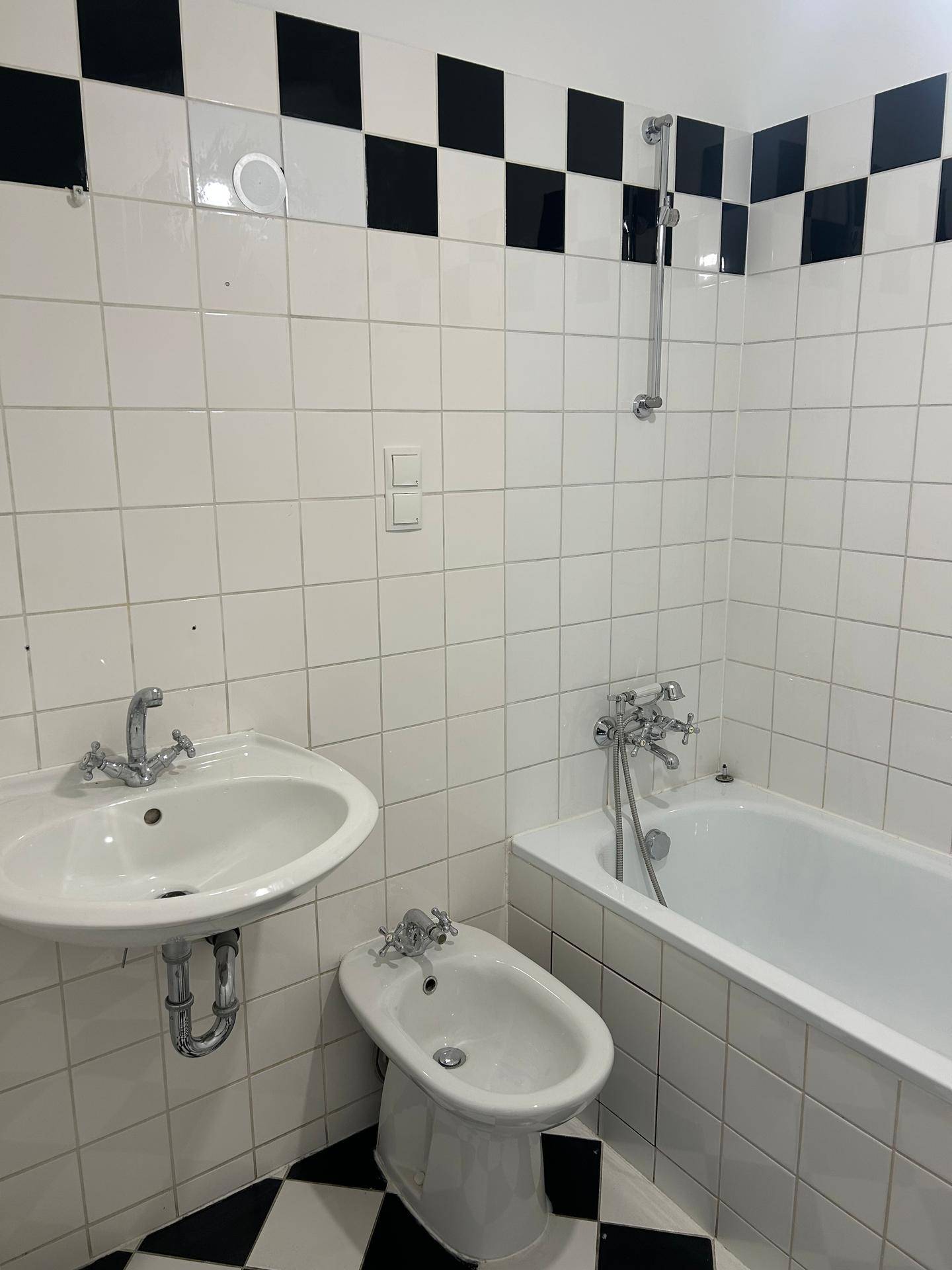 Badezimmer mit schwarz-weißen Fliesen, Badewanne, Waschbecken und Bidet.