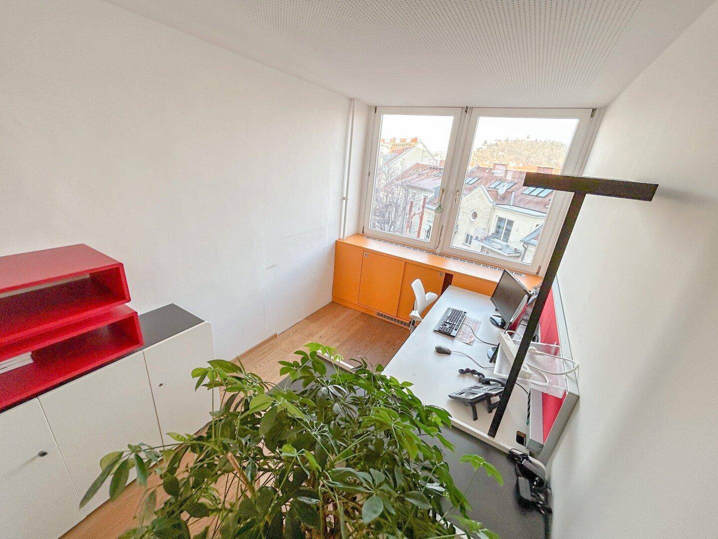 Kleines Büro mit einem Arbeitsplatz, Holzfußboden und Blick auf die Dächer der Stadt.