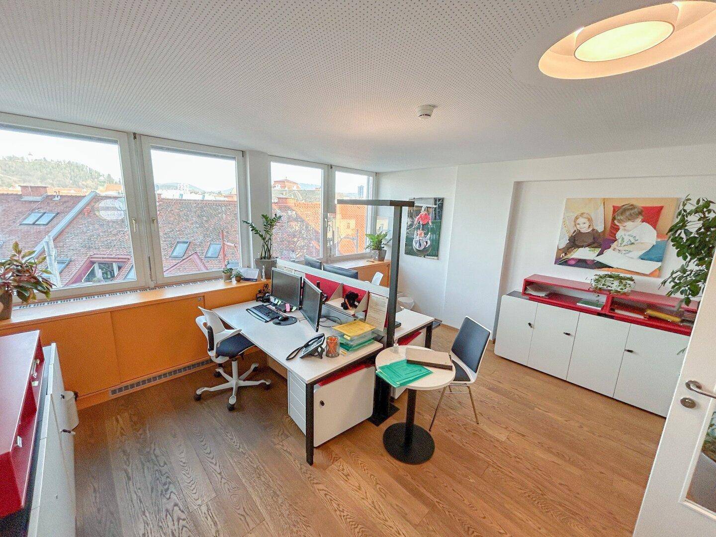Geräumiges Büro mit mehreren Schreibtischen, Holzfußboden und Blick auf die Stadt.