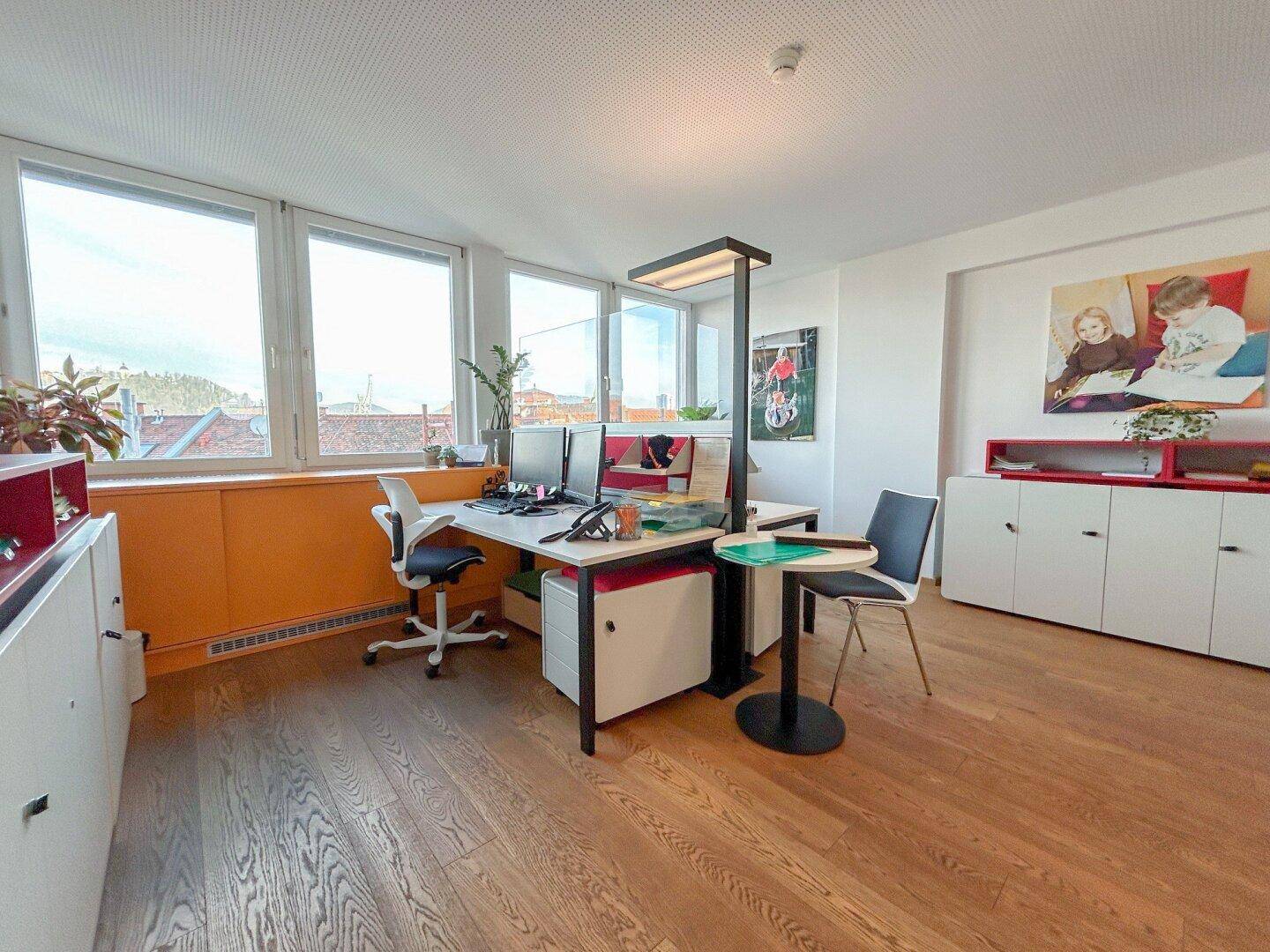 Helles Büro mit zwei Arbeitsplätzen, Holzfußboden und großen Fenstern mit Stadtblick.