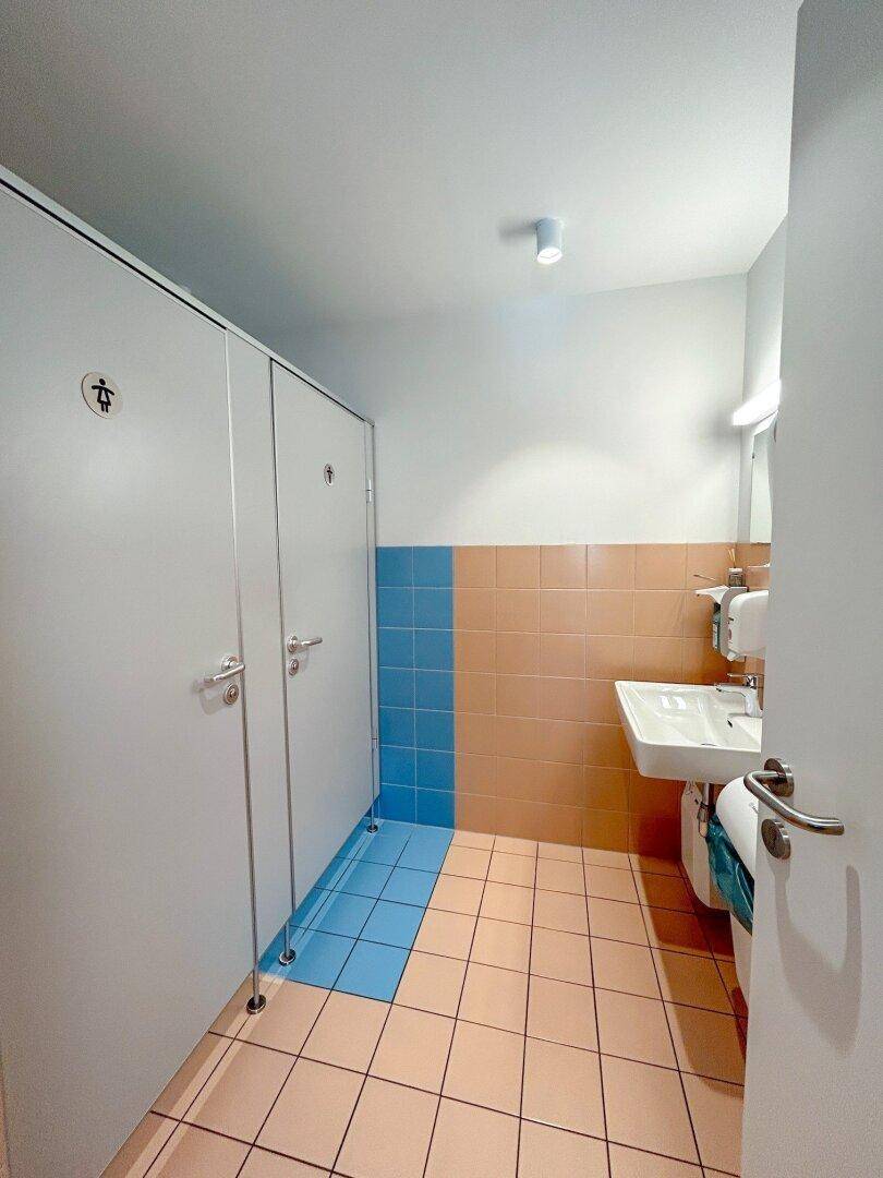 Toilettenraum mit Kabinen, Waschbecken und Spiegel, sauber und funktional.