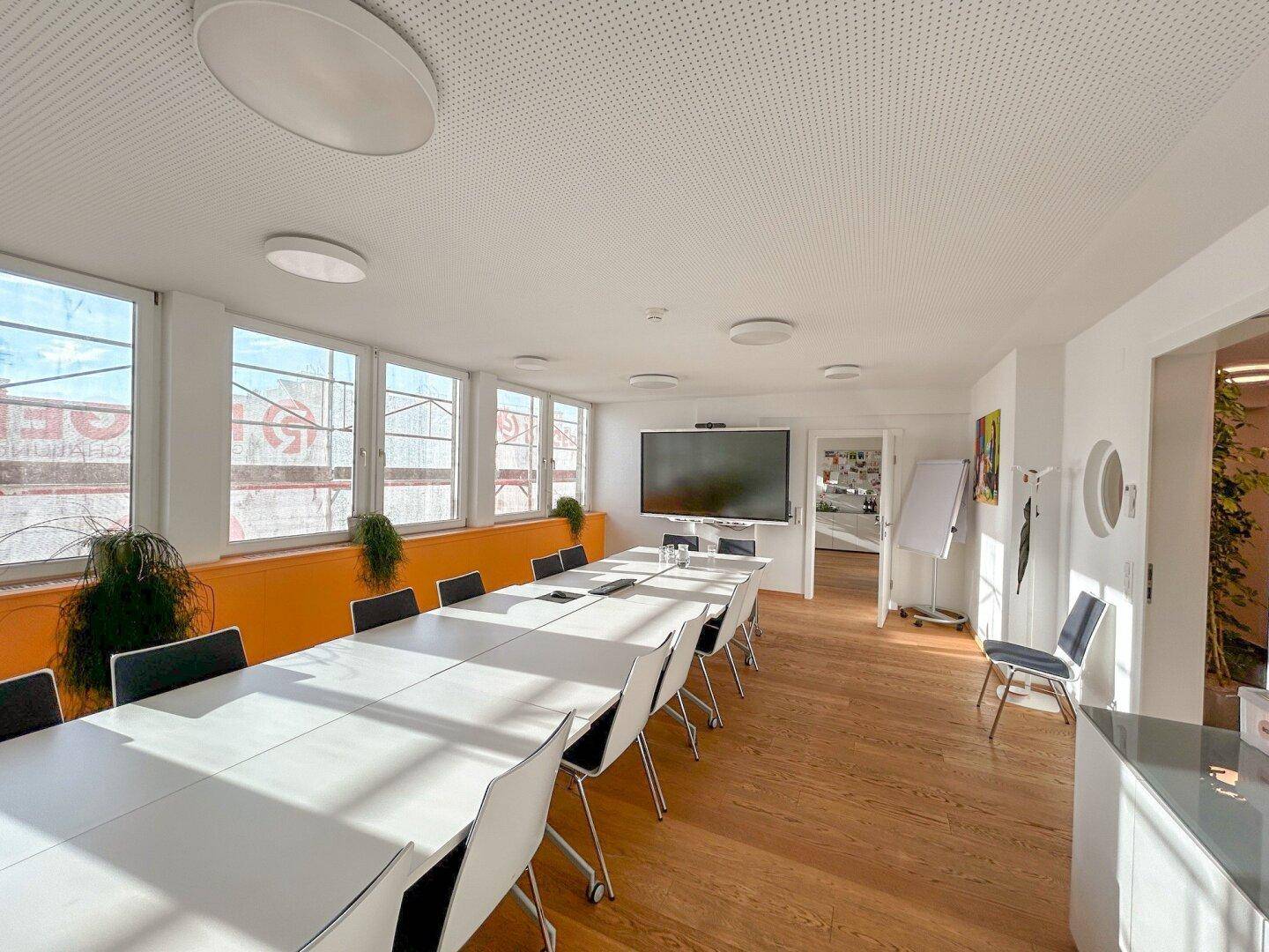 Geräumiger Konferenzraum mit langem Tisch, Stühlen und einem großen Bildschirm an der Wand.