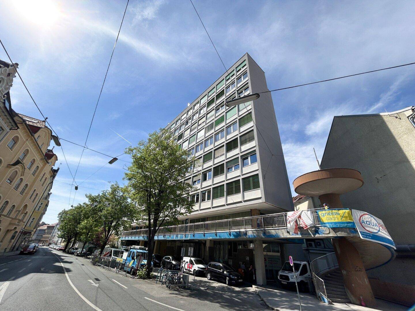 Modernes Hochhaus mit vielen Fenstern und Geschäften im Erdgeschoss, an einer belebten Stadtstraße gelegen.
