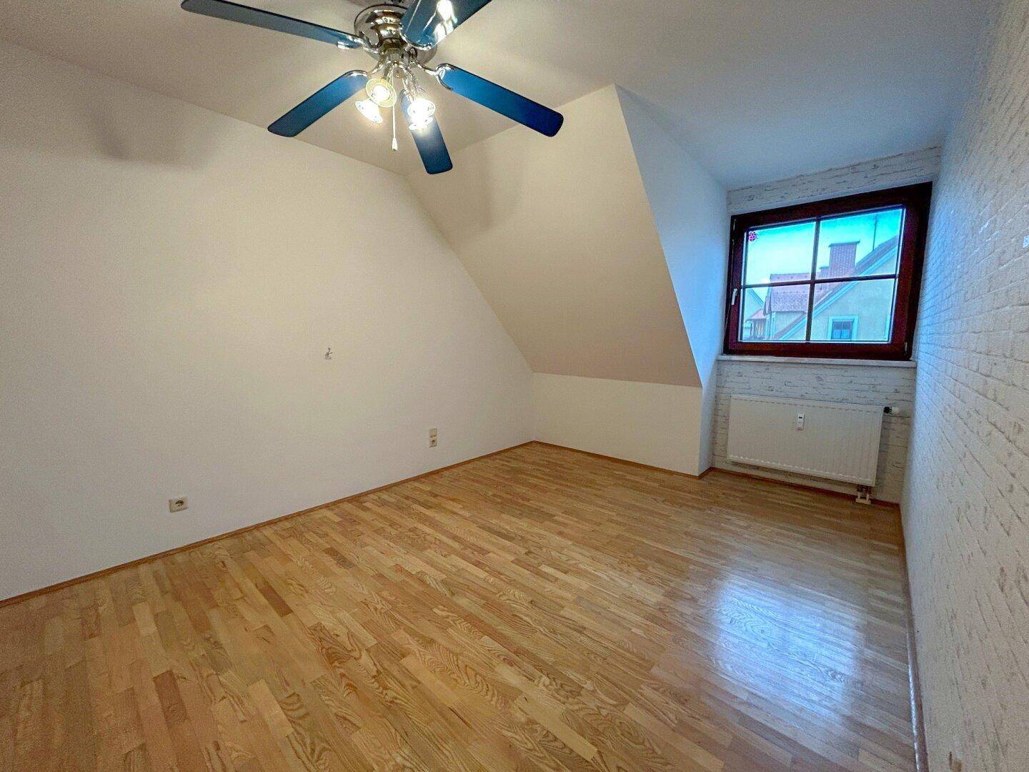 Gemütliches Schlafzimmer mit Parkettboden, Dachschräge und Deckenventilator für angenehmes Klima.