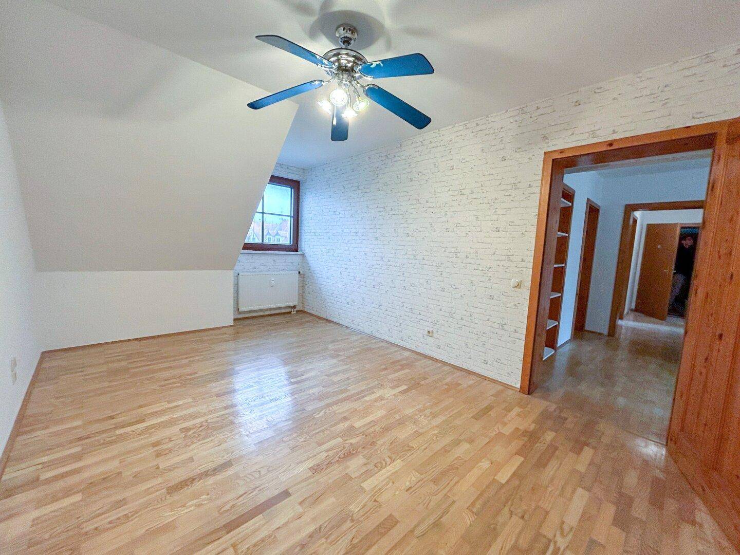 Helles Schlafzimmer mit Parkettboden, Deckenventilator und Zugang zu einem weiteren Raum.