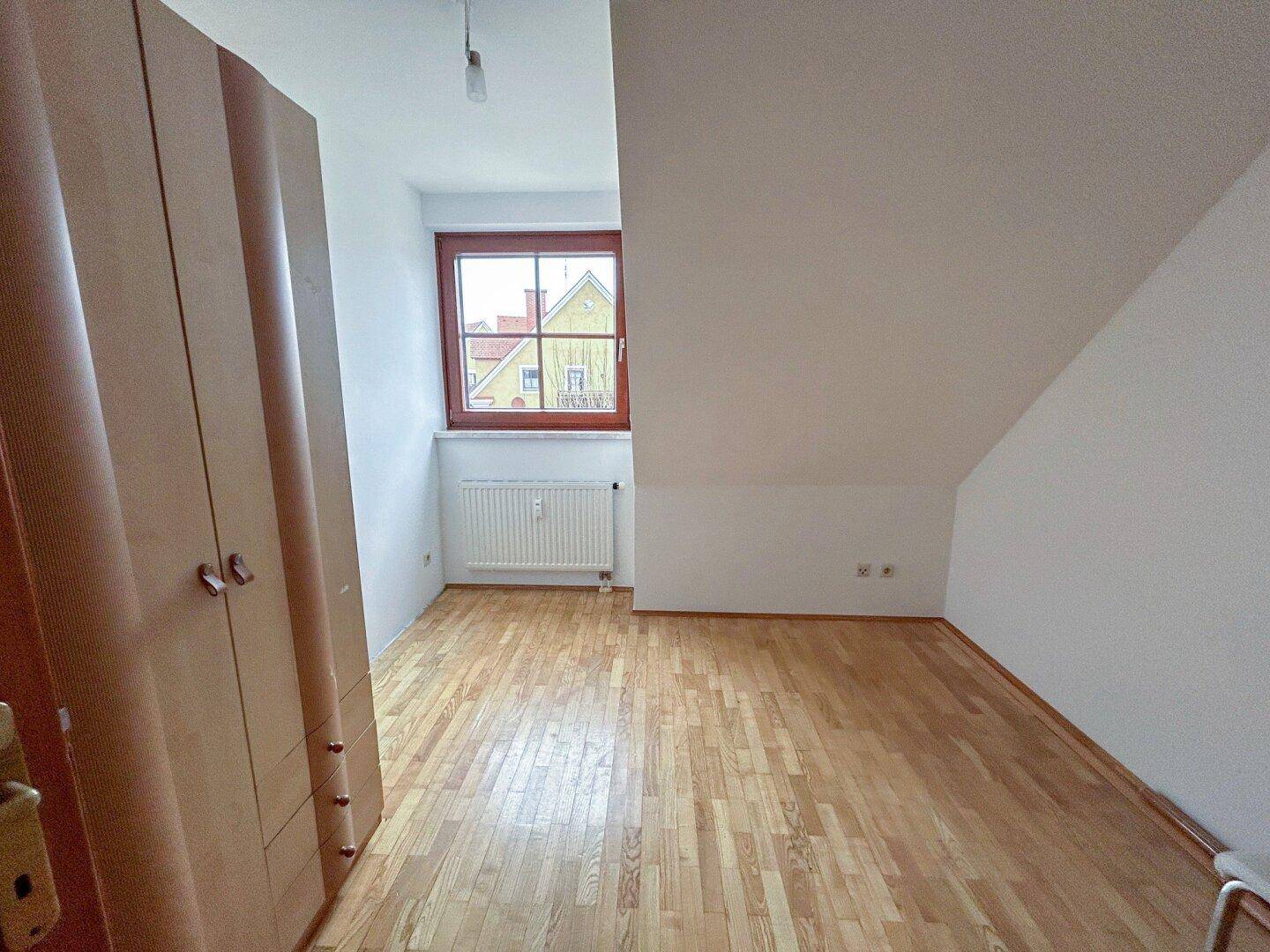 Schlafzimmer mit Parkettboden, Dachschräge und Fenster, bietet Platz für einen Kleiderschrank.