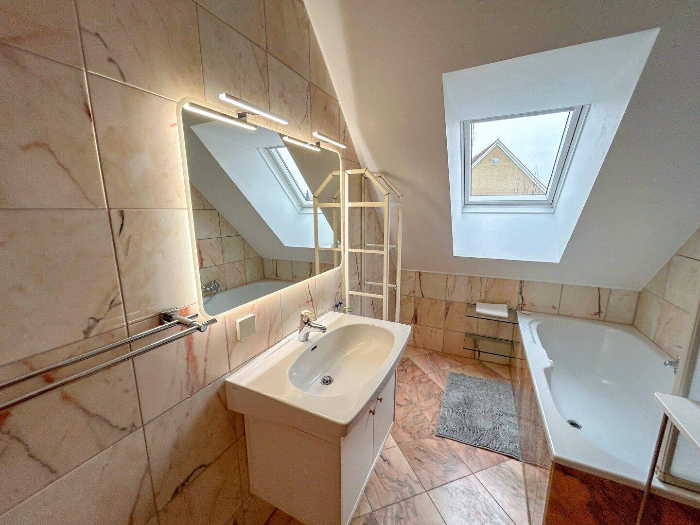 Modernes Badezimmer mit Marmorfliesen, Badewanne und Dachfenster für natürliches Licht.