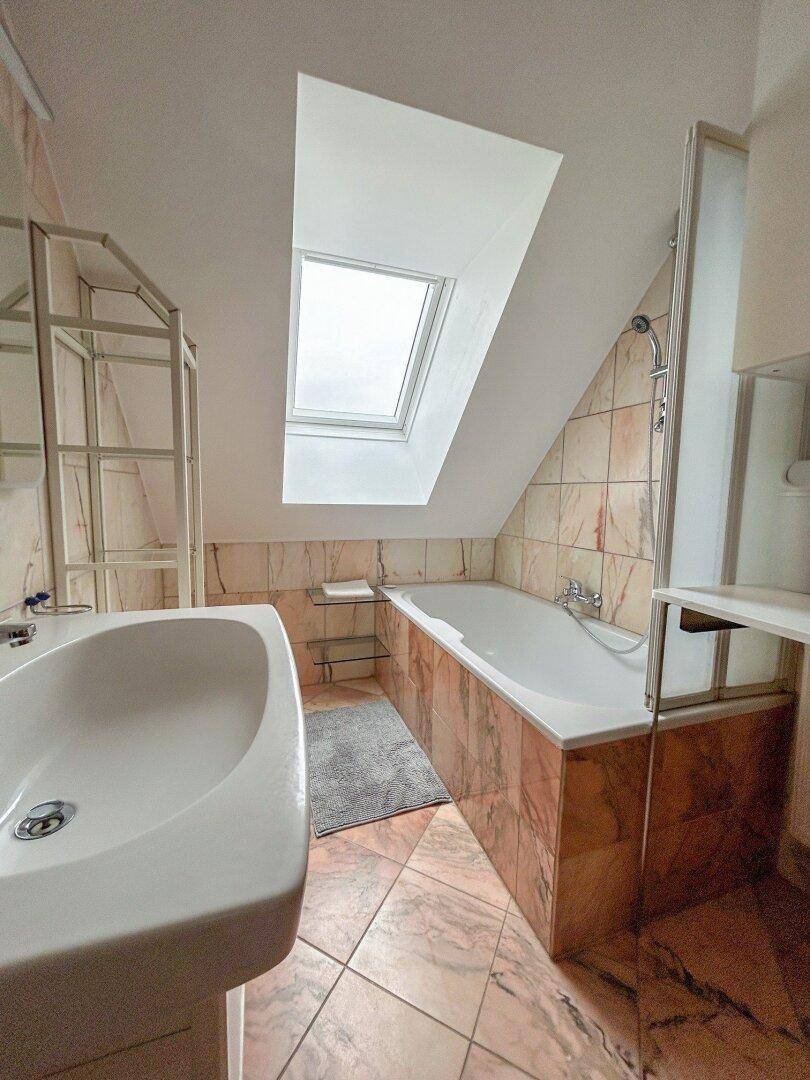 Badezimmer mit Badewanne, Dachfenster und Fliesen in warmen Farbtönen.