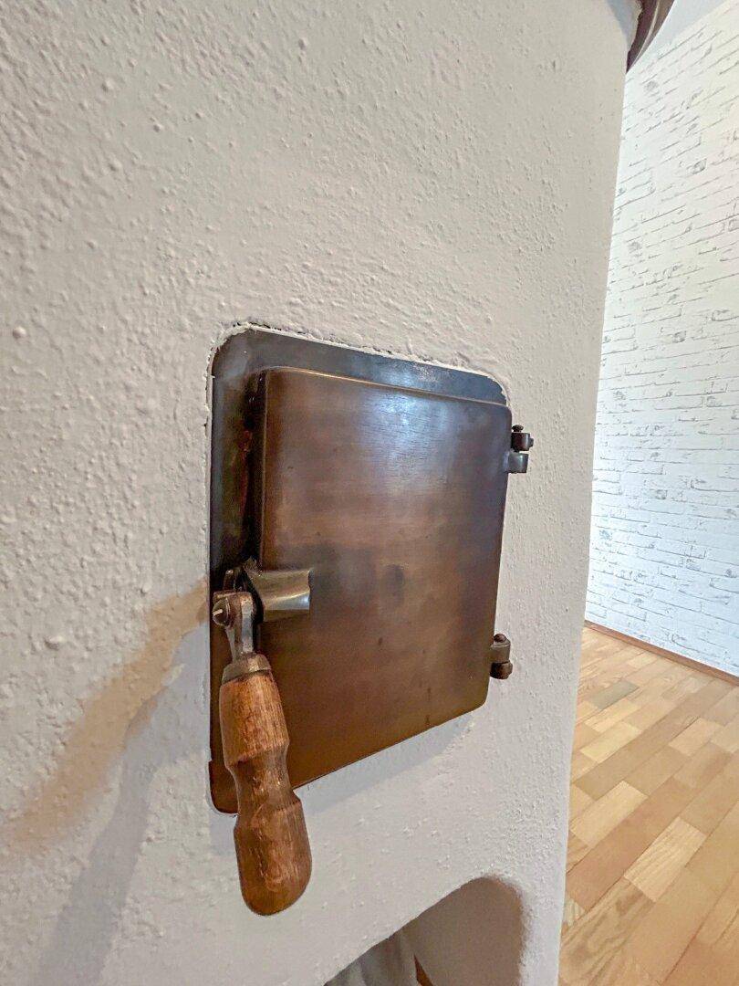 Nahaufnahme der gusseisernen Tür des traditionellen Kachelofens mit Holzgriff.