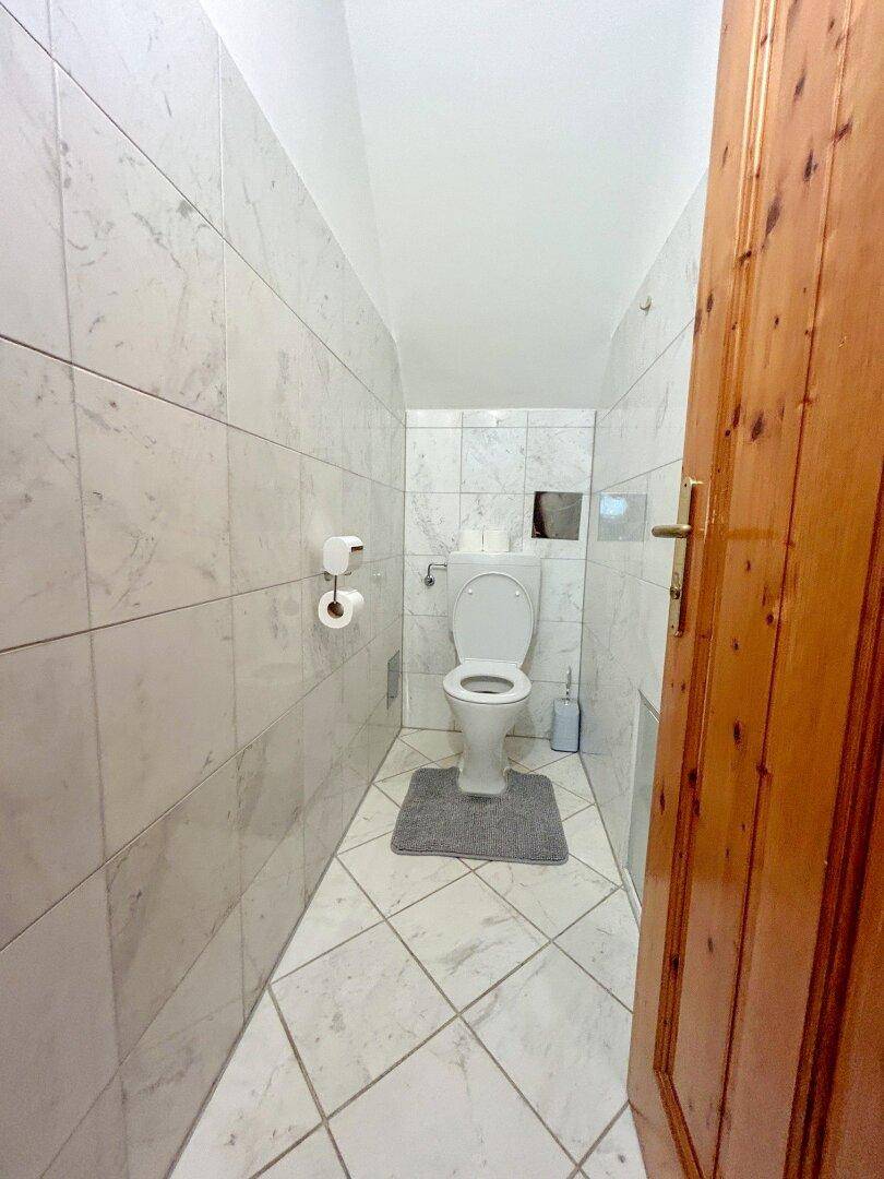 Separates WC mit hellen Fliesen und wandmontierter Toilette, praktisch und funktional.
