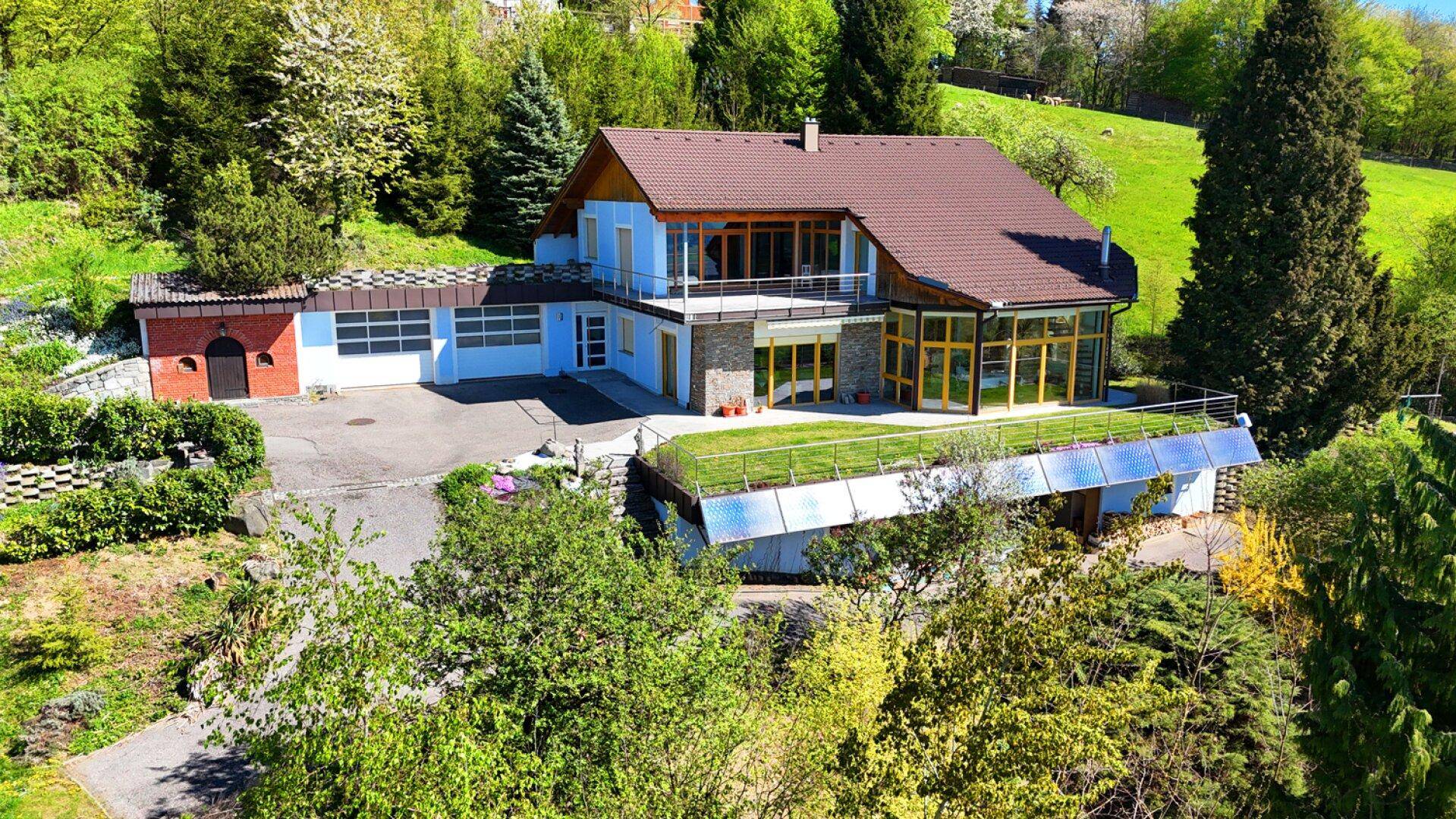 Luftaufnahme des Hauses mit blauer Fassade, großzügigen Fensterfronten und grüner Umgebung.