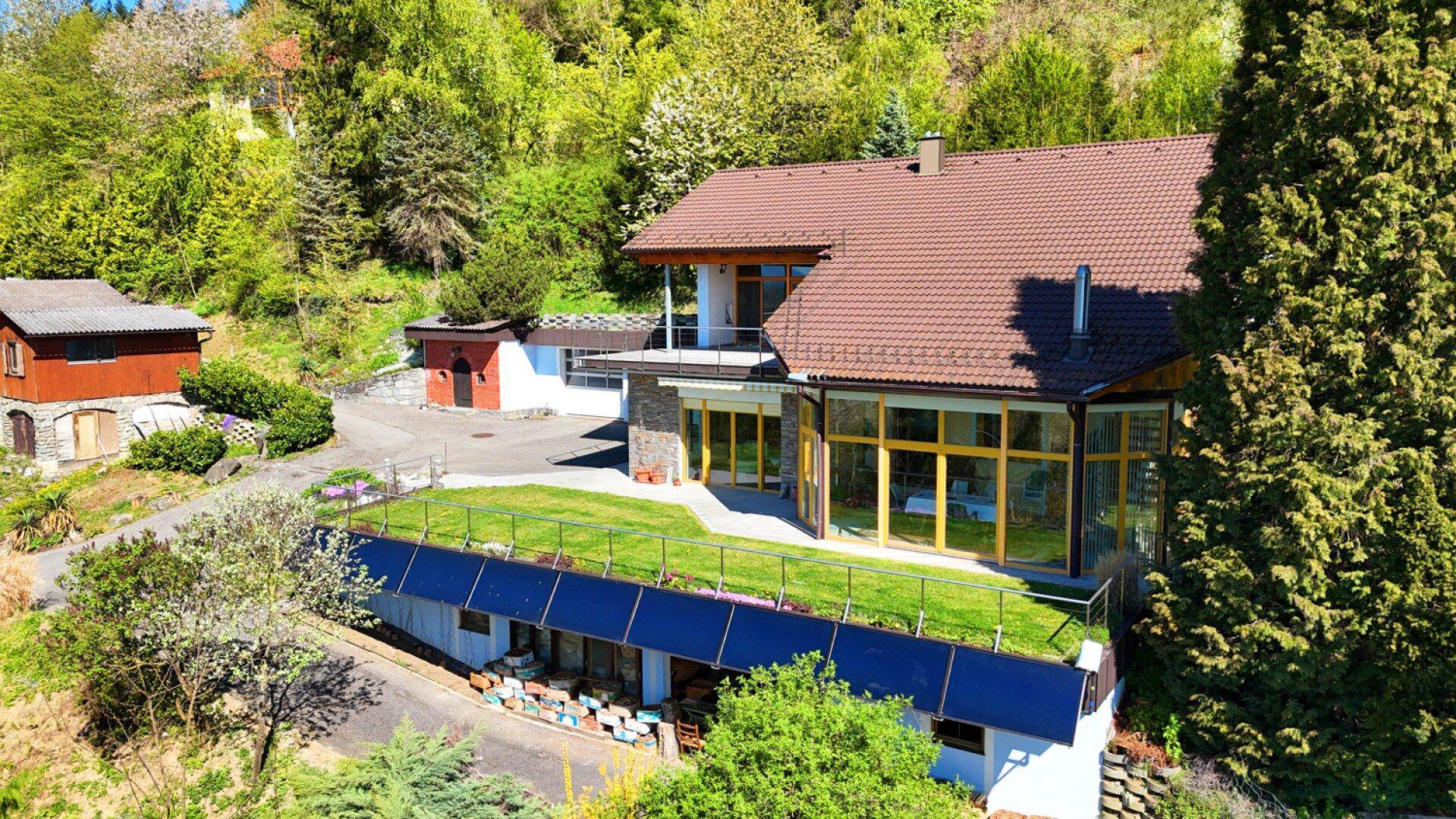 Ansicht des Hauses von oben mit braunem Dach, großen Fenstern und einer grünen Dachterrasse.
