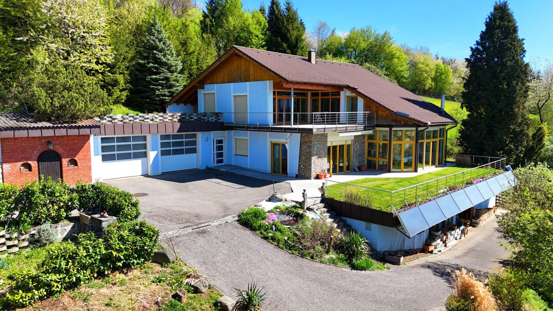 Luftaufnahme des Hauses mit blauer Fassade, braunem Dach und einer großen Auffahrt.
