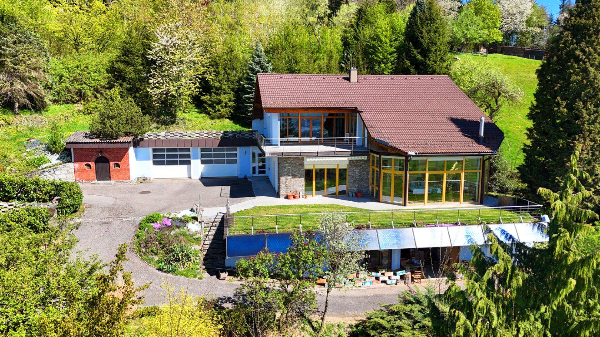 Luftaufnahme des Hauses mit blauer Fassade, braunem Dach und einer grünen Dachterrasse.