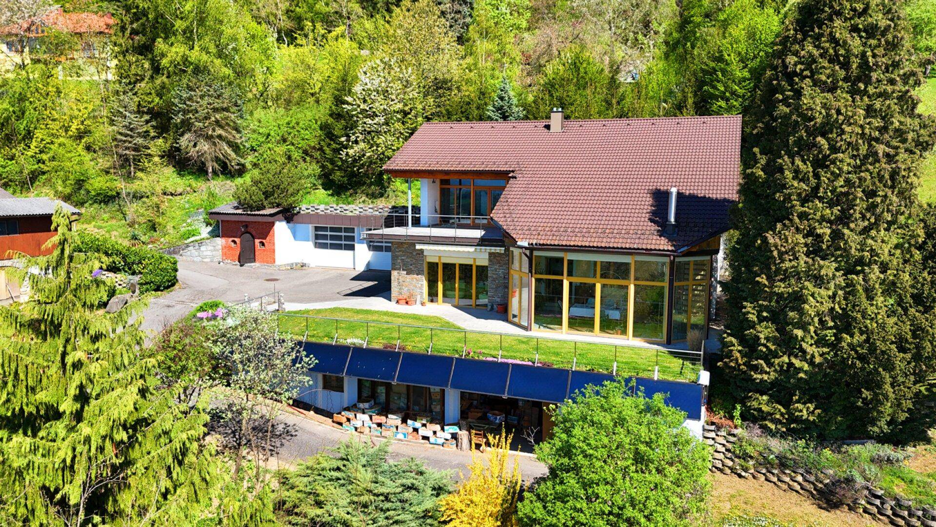 Luftaufnahme des Hauses mit blauer Fassade, braunem Dach und einer grünen Dachterrasse.