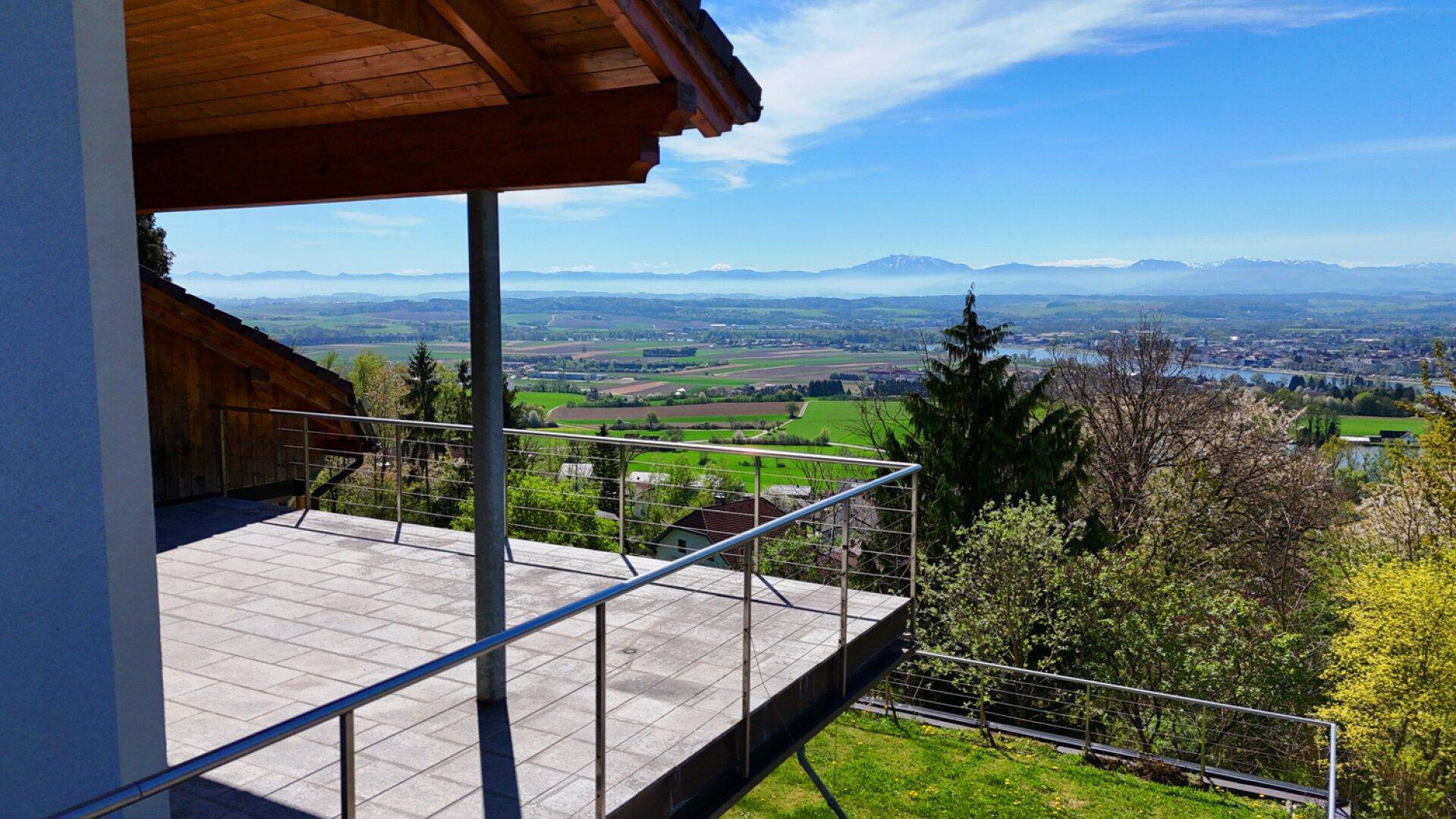 Überdachter Balkon mit Edelstahlgeländer und weitem Blick über die grüne Landschaft und Berge.