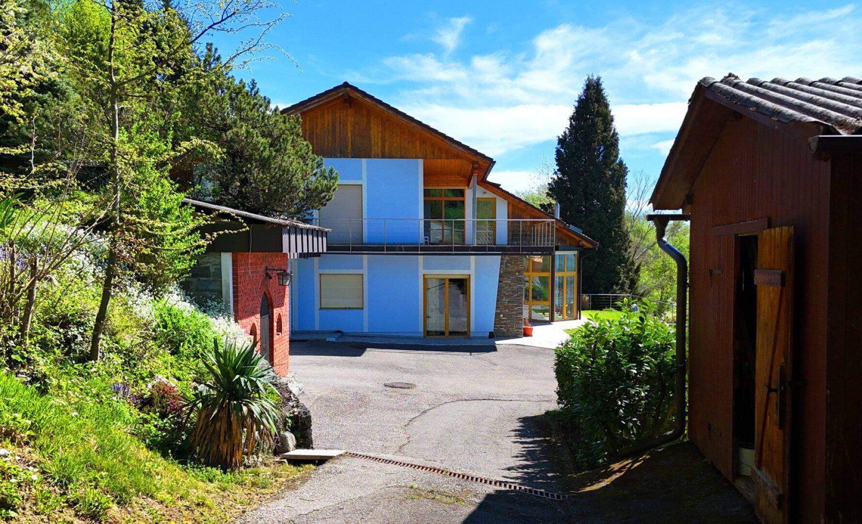 Ansicht des Hauses von der Auffahrt aus, umgeben von Bäumen und Sträuchern.