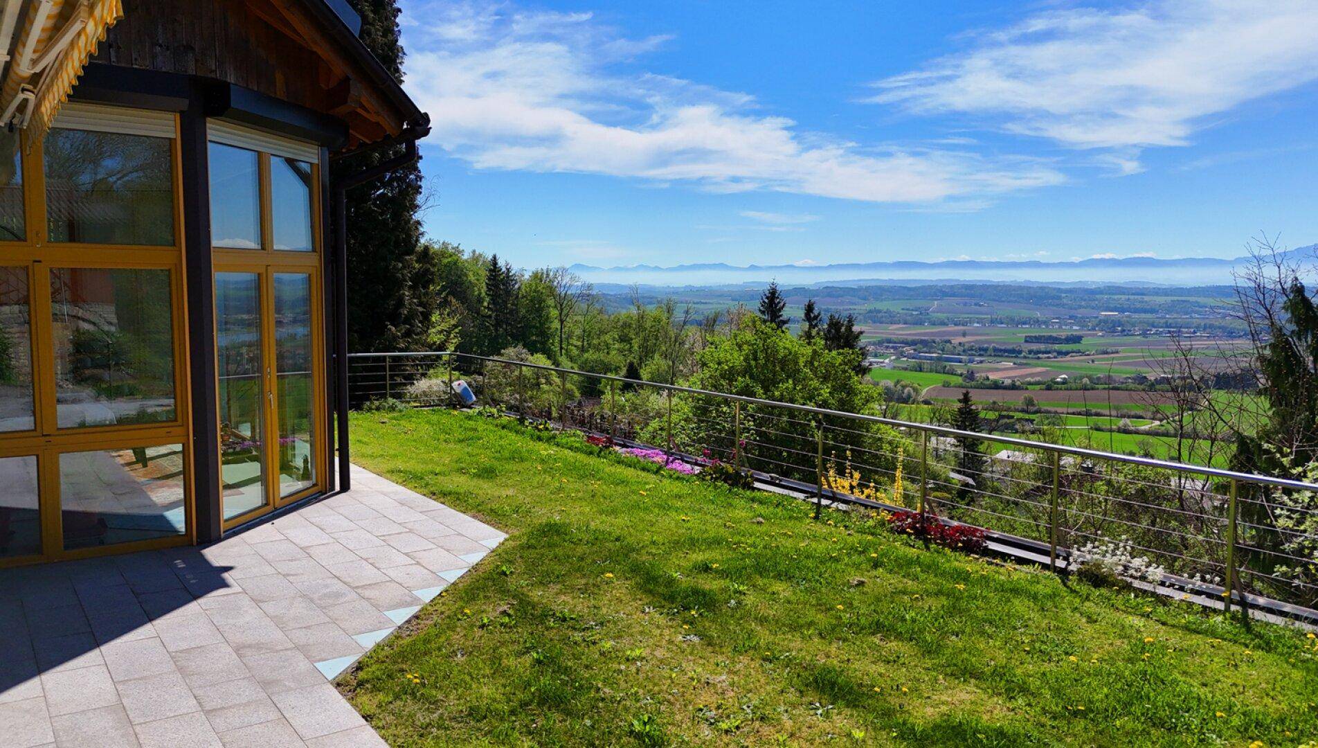 Gepflasterte Terrasse und Rasenfläche mit weitem Blick über die grüne Landschaft und Berge.