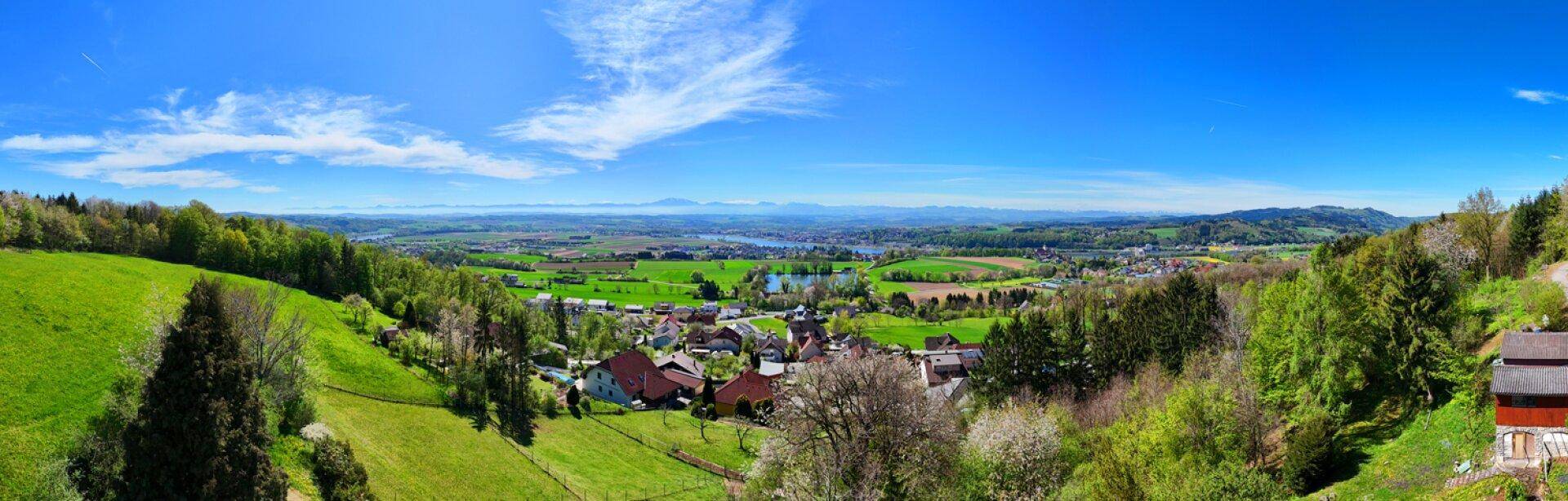 Weitläufiger Panoramablick über eine grüne Landschaft mit Seen, Dörfern und fernen Bergen.