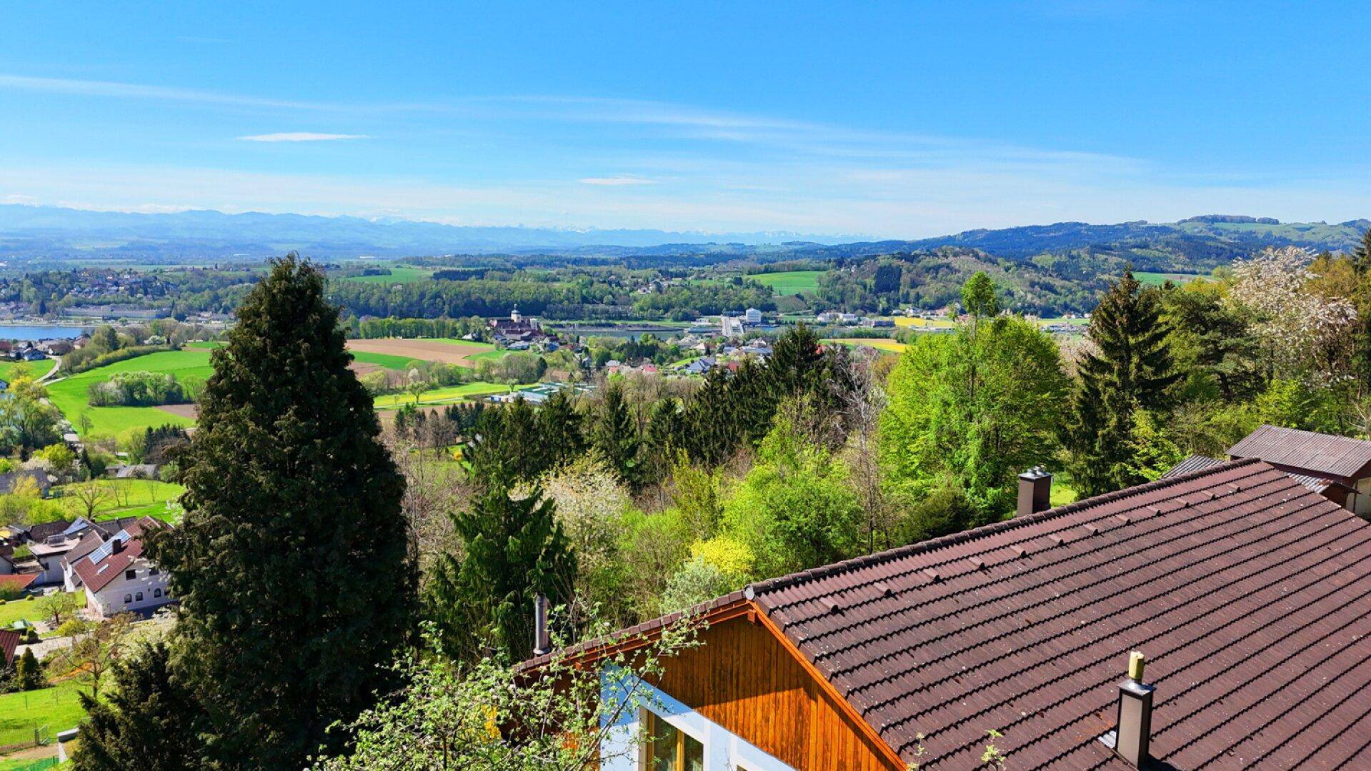 Blick über das Dach des Hauses auf die weite grüne Landschaft mit Seen und Bergen.