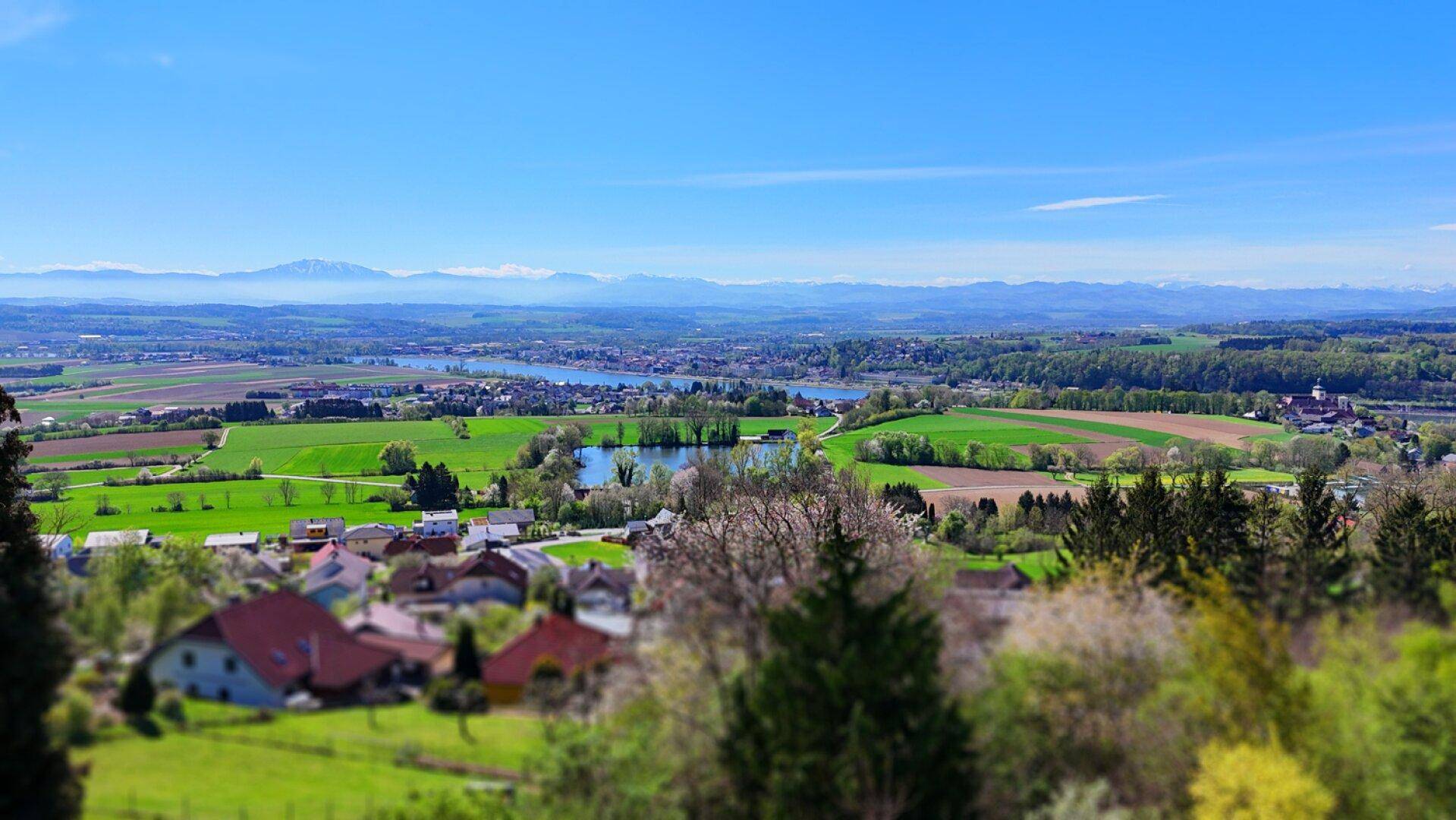 Weitläufiger Panoramablick über eine grüne Landschaft mit Seen, Dörfern und fernen Bergen.