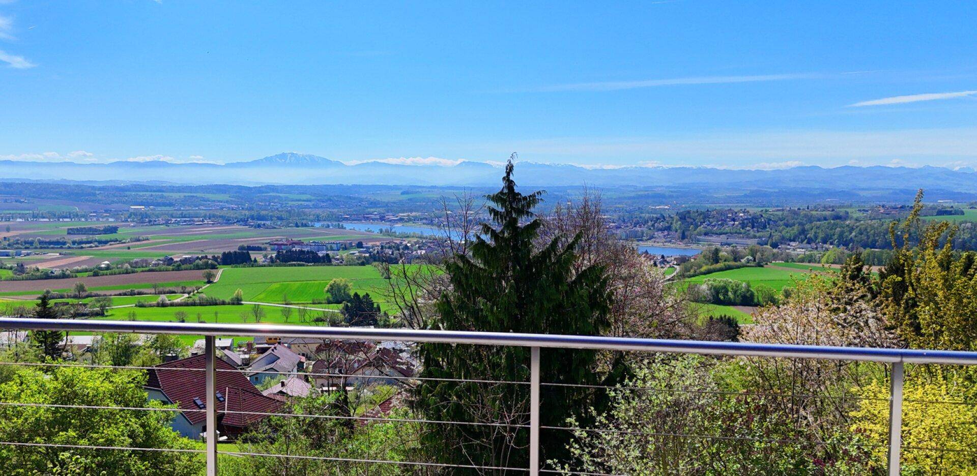 Panoramablick über die grüne Landschaft mit Seen und fernen Bergen, hinter einem Geländer.