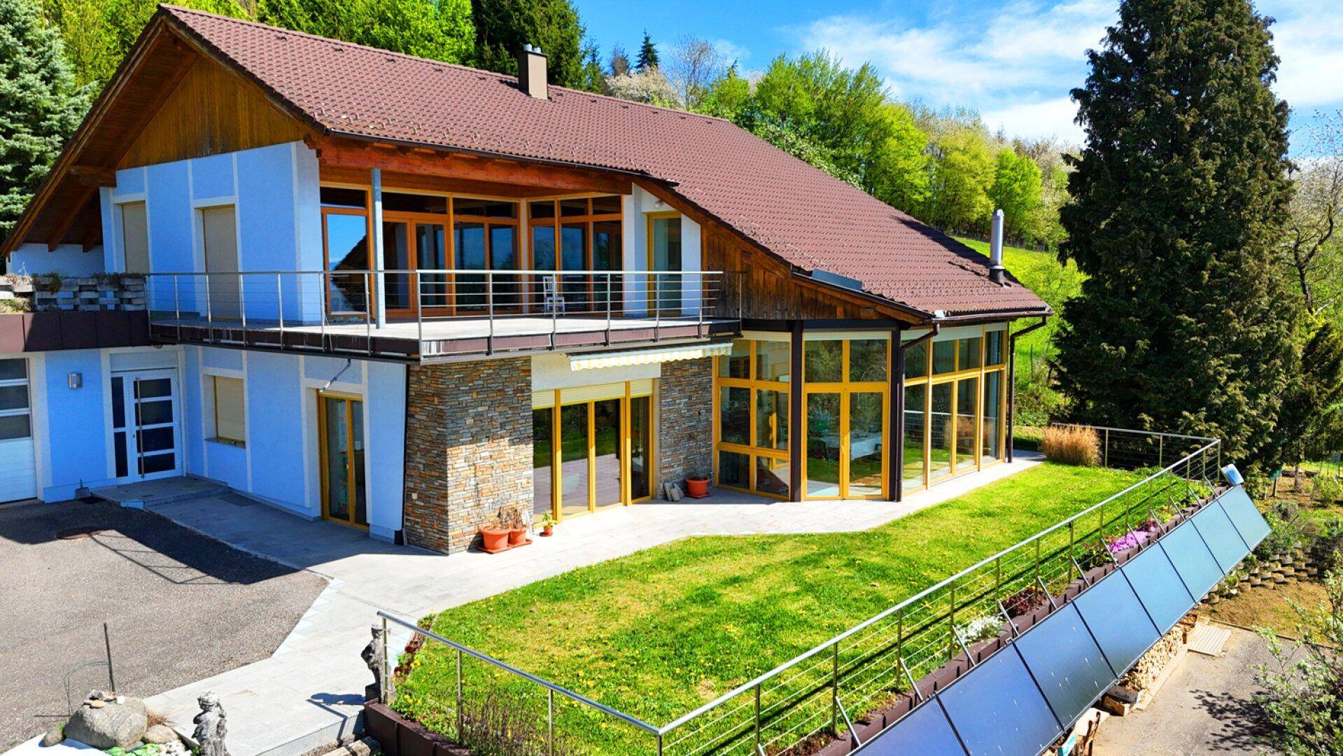 Luftaufnahme des Hauses mit blauer Fassade, braunem Dach und einer grünen Dachterrasse.