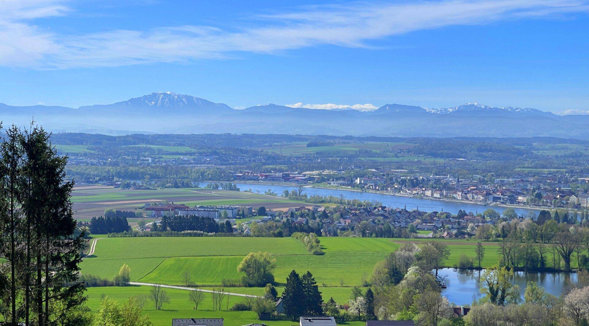 Weitläufiger Panoramablick über eine grüne Landschaft mit Seen, Dörfern und fernen Bergen.