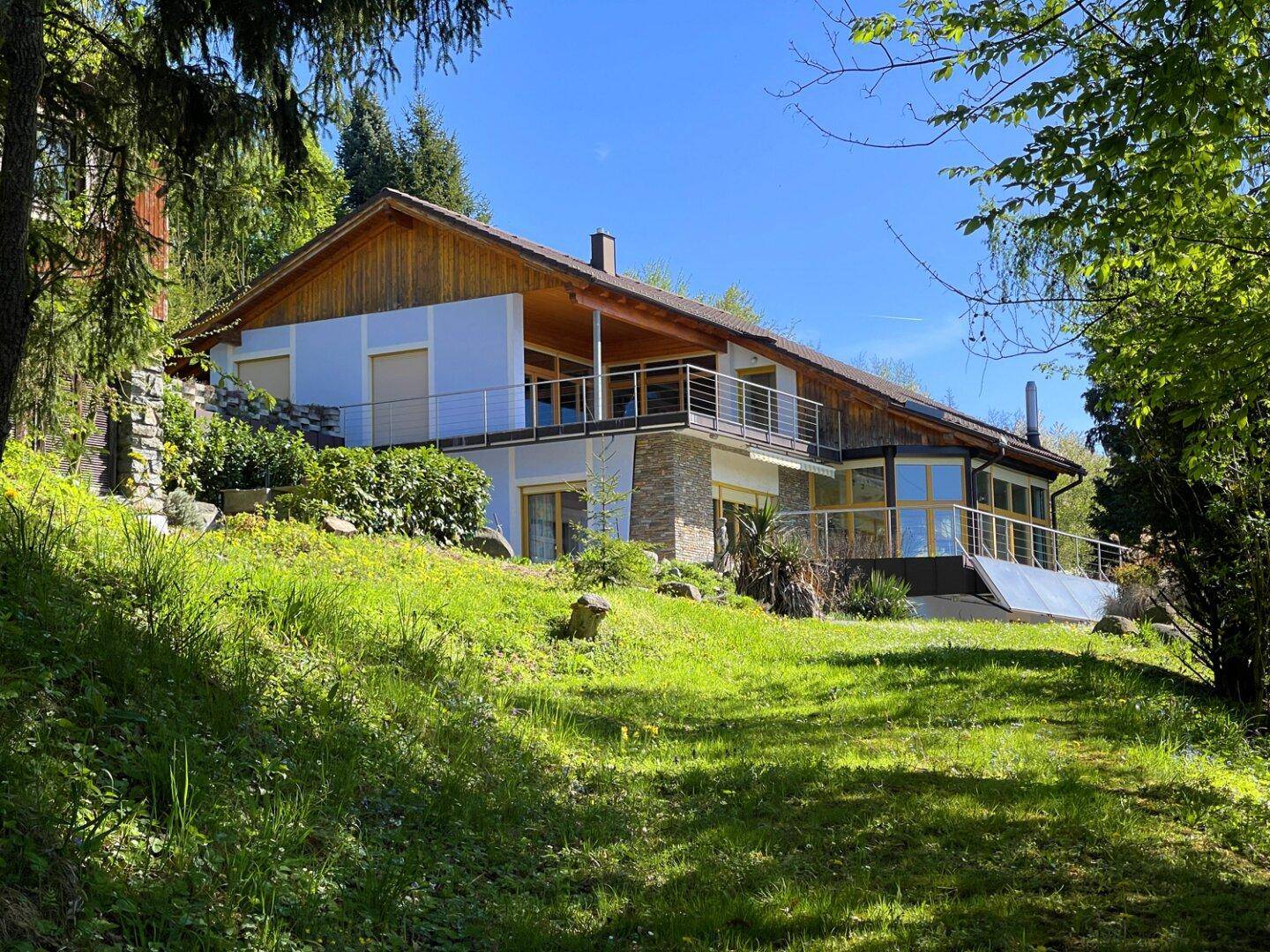 Großzügiges Haus mit Holzverkleidung und mehreren Balkonen, eingebettet in eine grüne Landschaft.