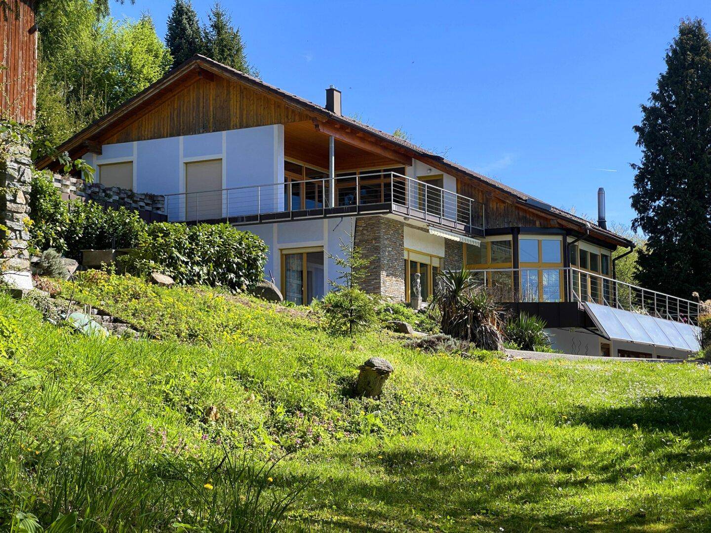 Detailansicht des Hauses mit Holzfassade, Steinakzenten und großen Fensterfronten.