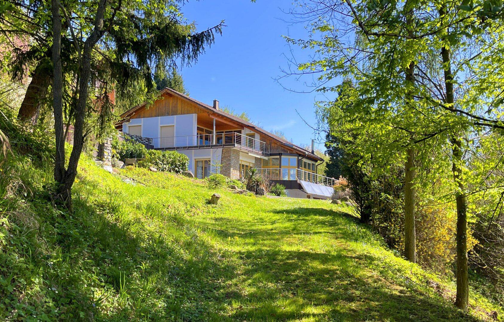 Freistehendes Haus mit moderner Architektur und weitläufigen Grünflächen unter blauem Himmel.