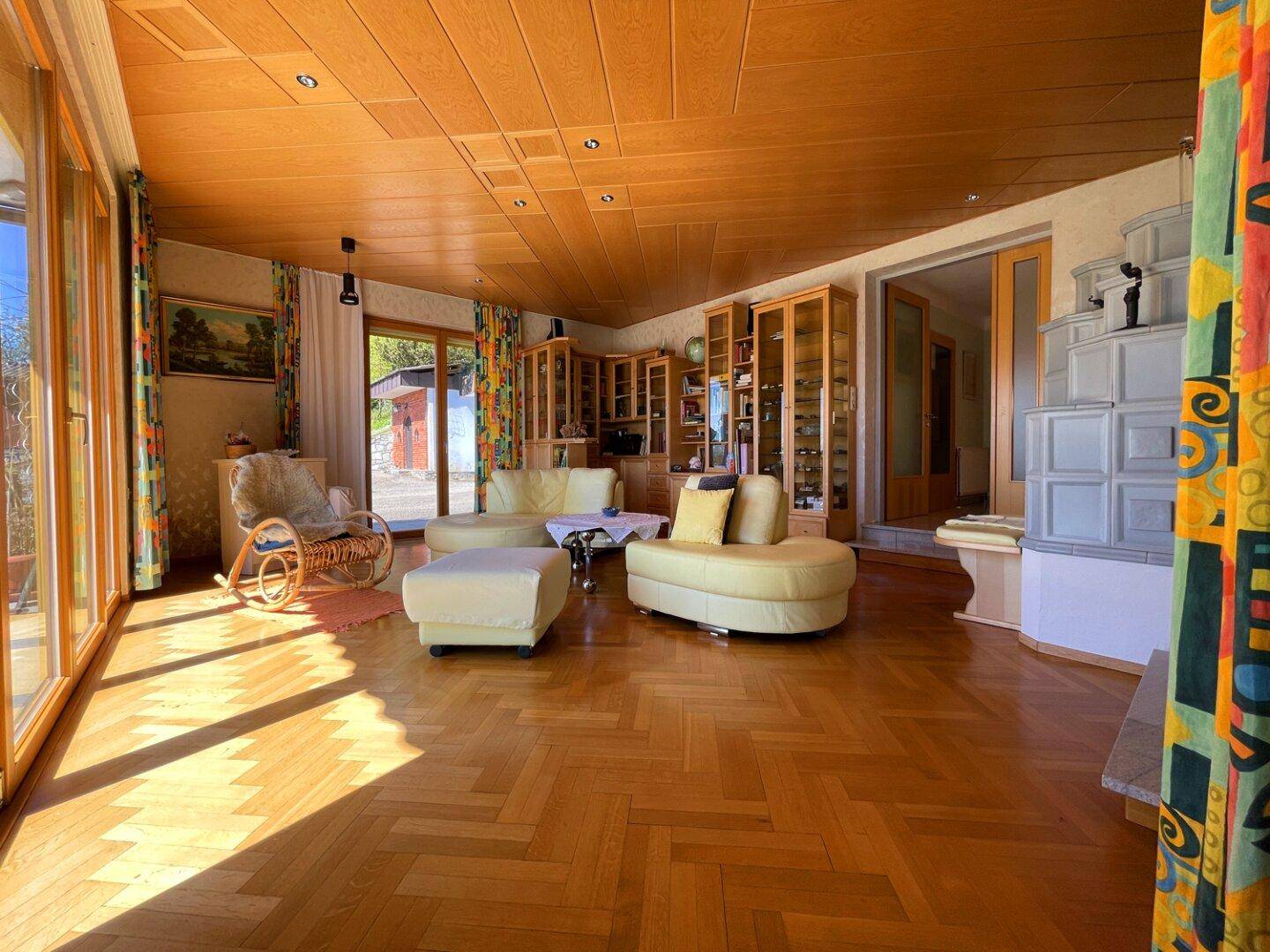 Gemütliches Wohnzimmer mit traditionellem Kachelofen, Holzdecke und Parkettboden.