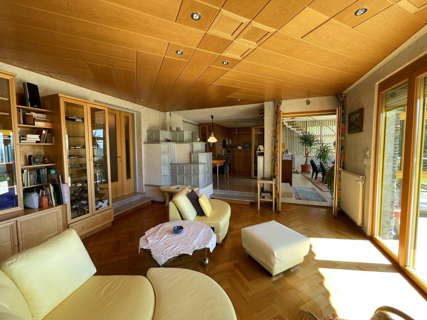 Helles Wohnzimmer mit Holzdecke, Parkettboden und integrierten Vitrinen, die zum Essbereich führen.