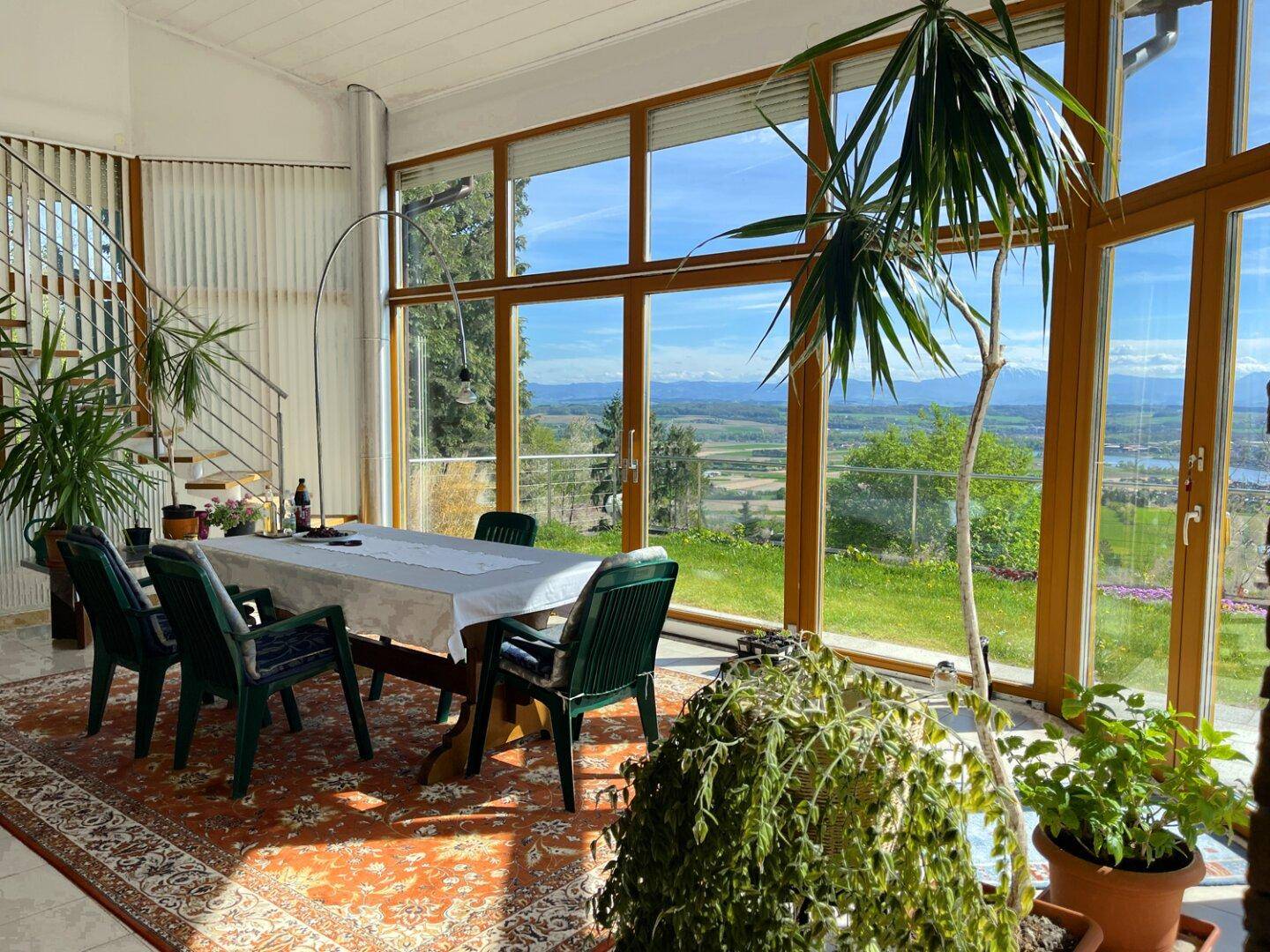 Geräumiger Wintergarten mit Esstisch, vielen Pflanzen und einem beeindruckenden Panoramablick.