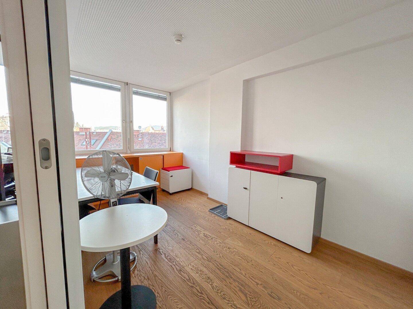 Büroraum mit Holzboden, Schränken und einem Ventilator, der für Kühlung sorgt.