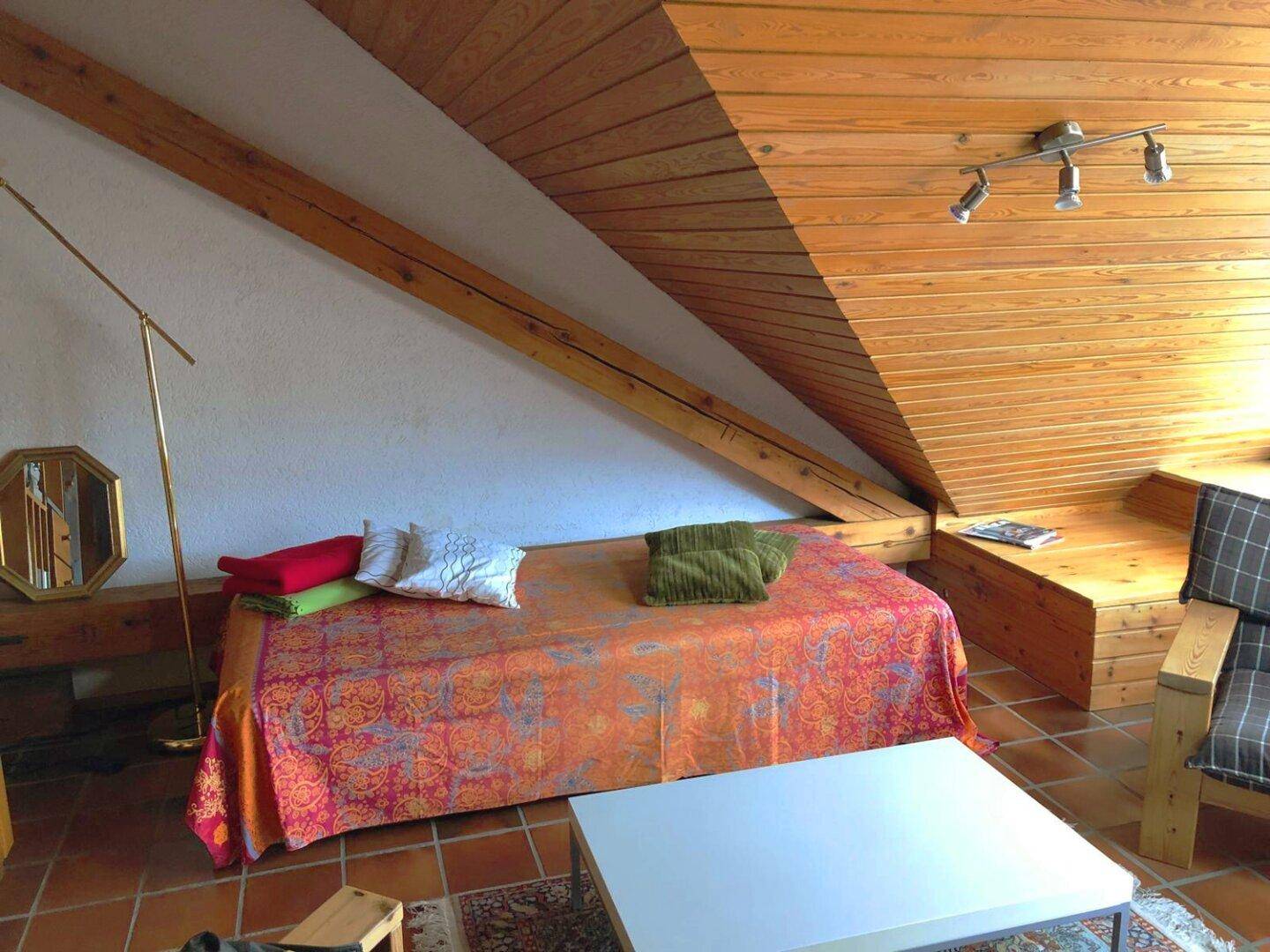 Heller Dachbodenraum mit Holztäfelung, Terrakottafliesen und einem Bett als Entspannungsbereich.