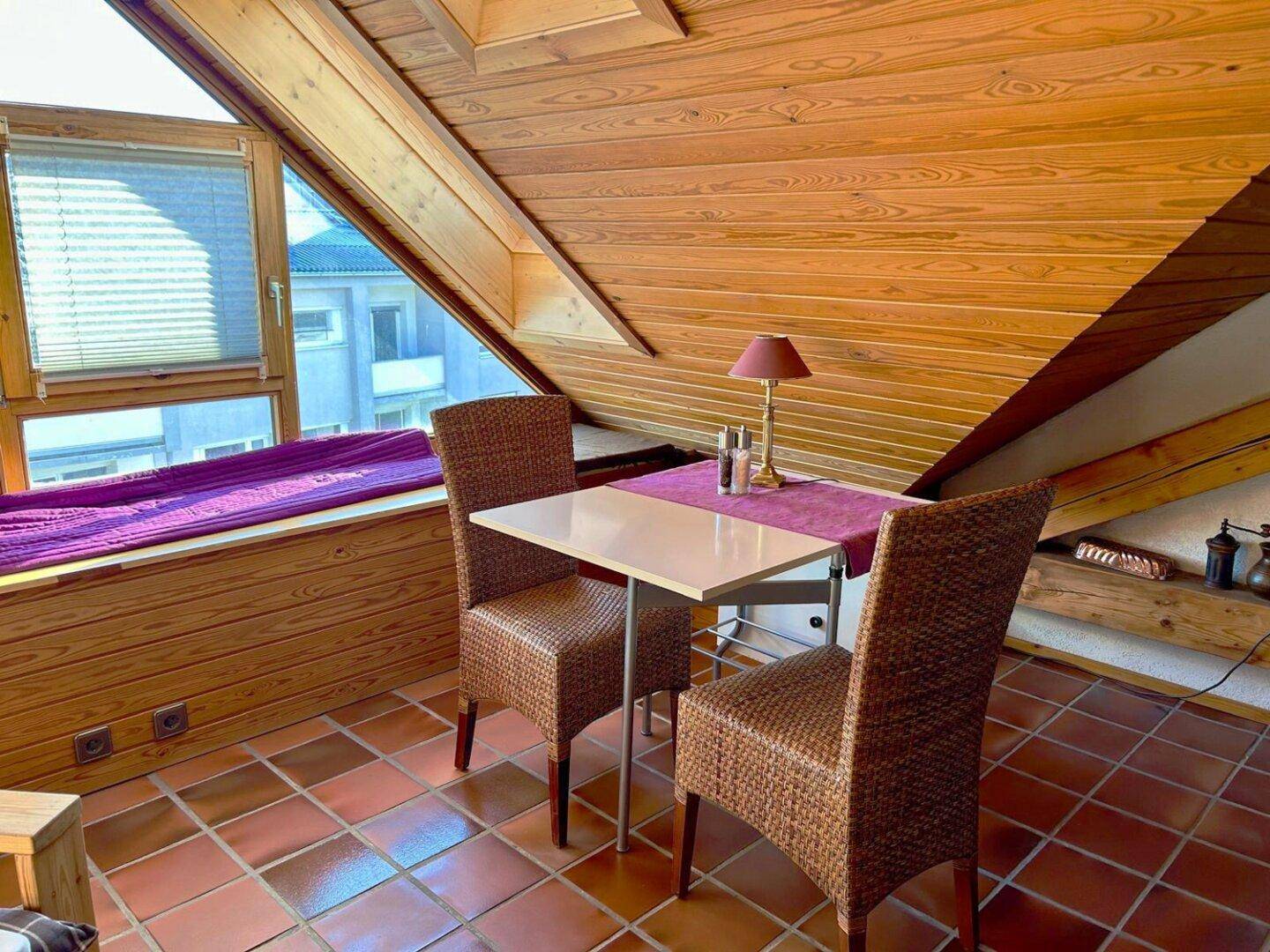 Gemütlicher Dachbodenbereich mit Holztäfelung, Terrakottafliesen und kleinem Esstisch am Fenster.